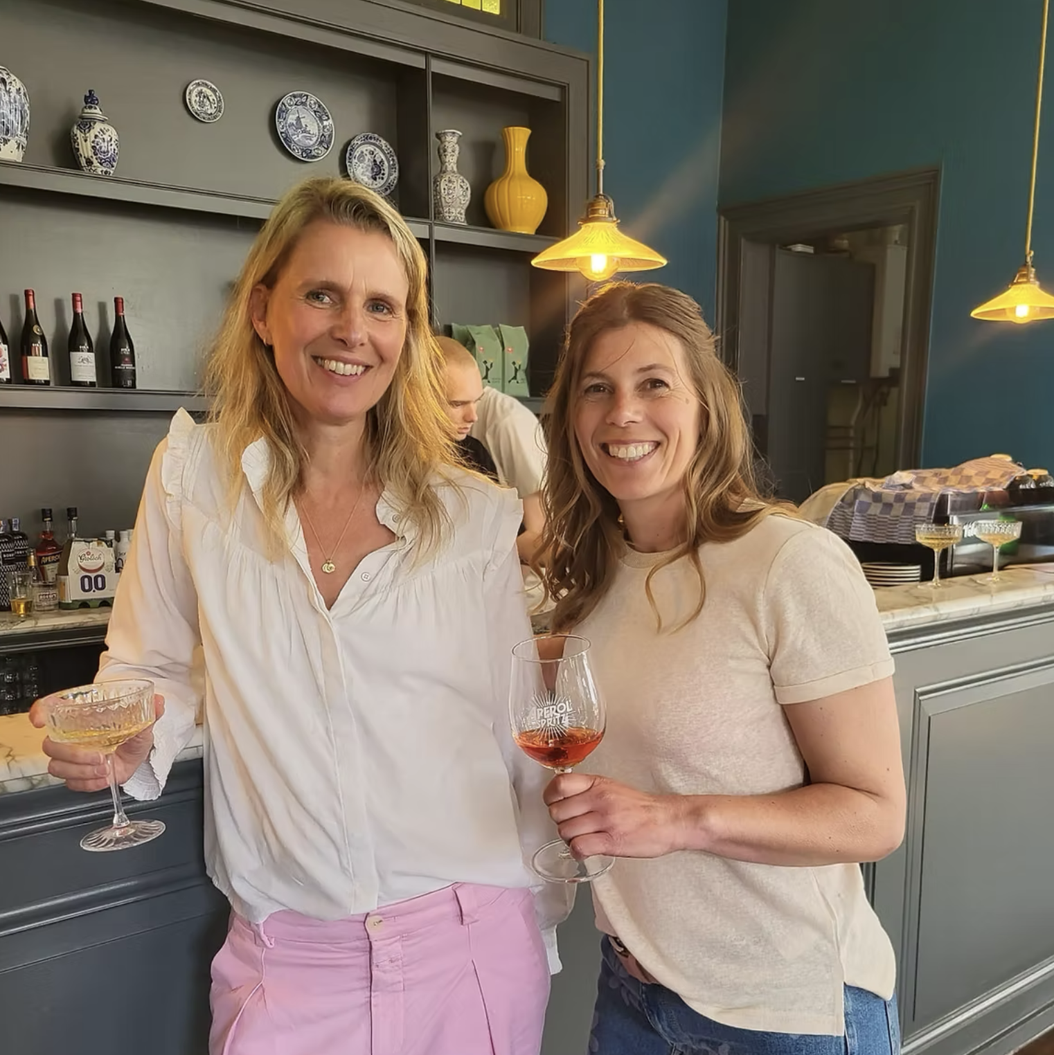 Twee vrouwen glimlachen en houden een glas wijn, terwijl ze in een restaurant of bar staan.