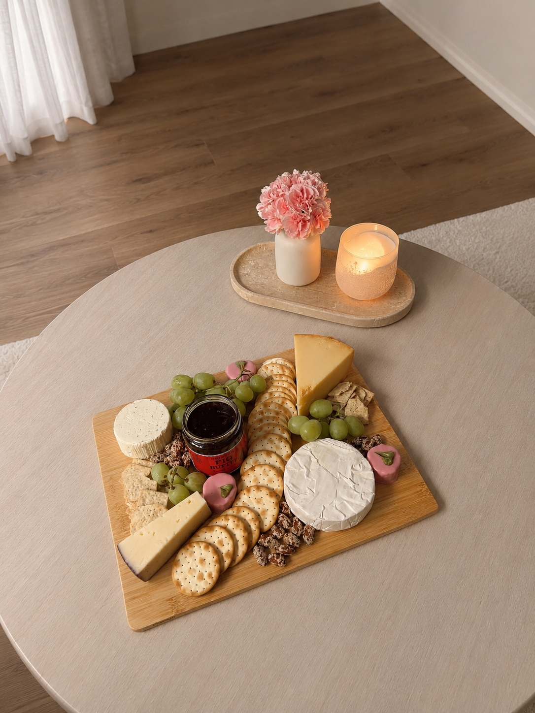 Charcuterie board with cheese, fruit, crackers, and jam on a wooden board.