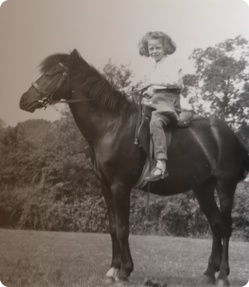 A young girl with curly hair riding a horse outdoors during daytime, with trees in the background.