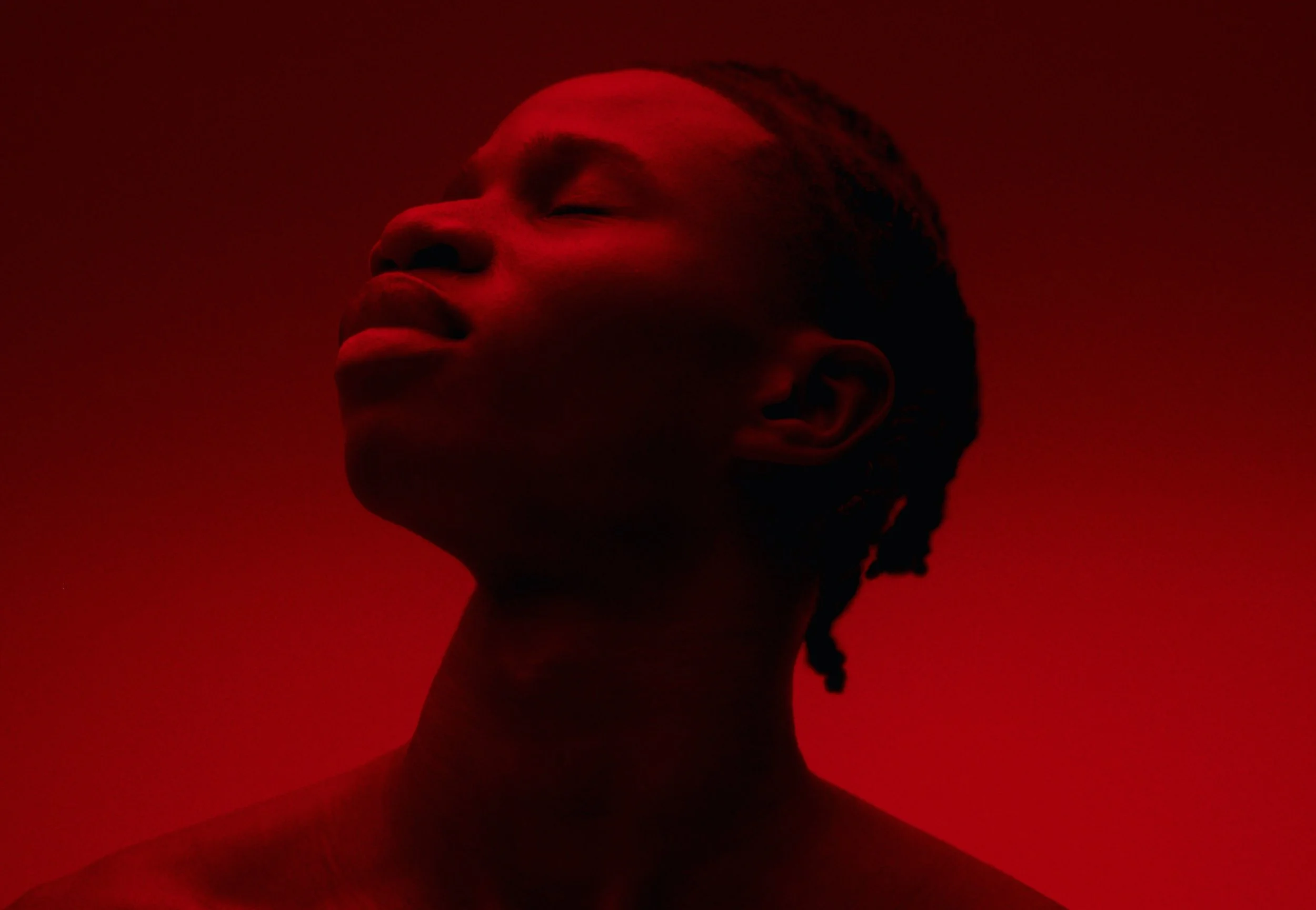 Profile of a woman with closed eyes, lit in red light, with braided hair.