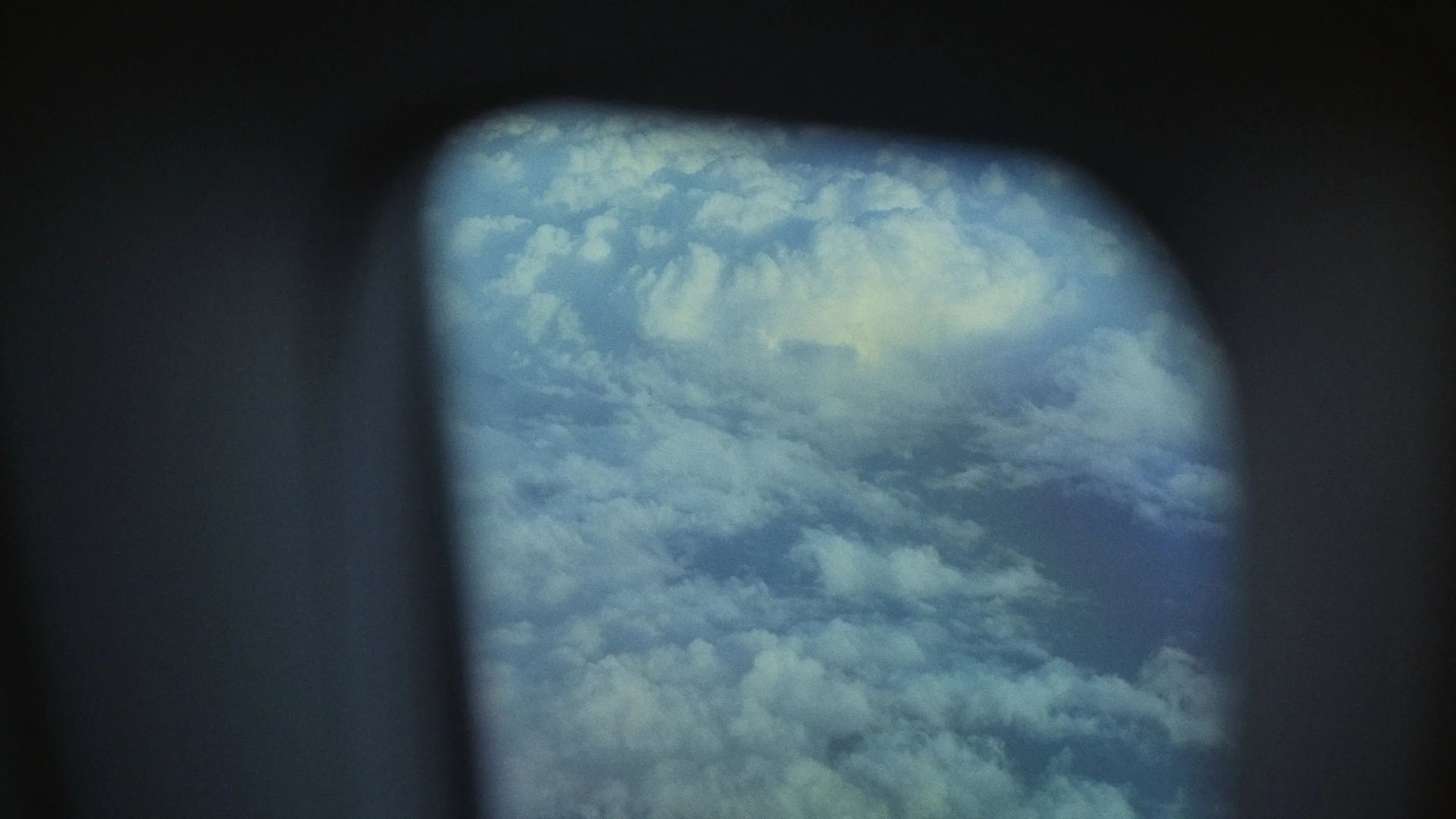 View of cloudy blue sky through a circular opening or lens, with dark framing around the edges.