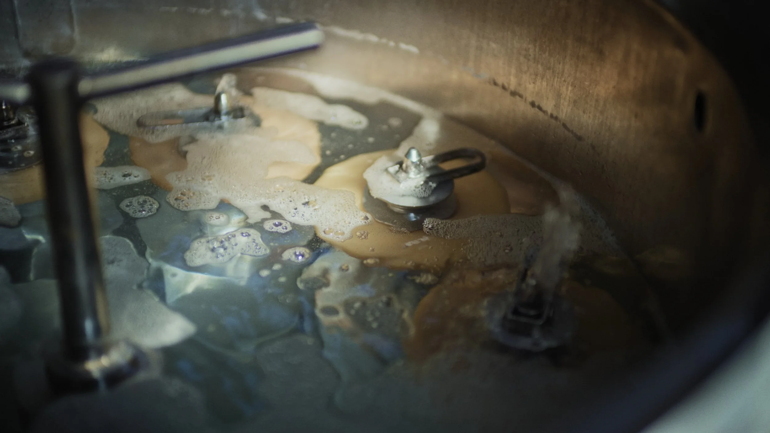 Close-up of a metal surface with soap bubbles and foam from a mechanical process, possibly involving washing or cleaning.