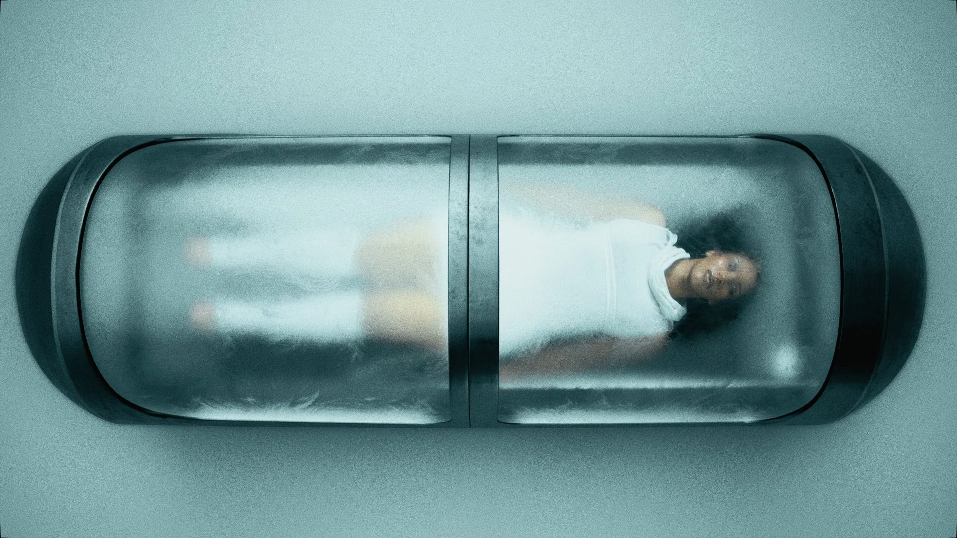 A woman lying inside a cylindrical stainless steel container, resembling a cryogenic or sterilization chamber, with a metallic surface and a viewer window.