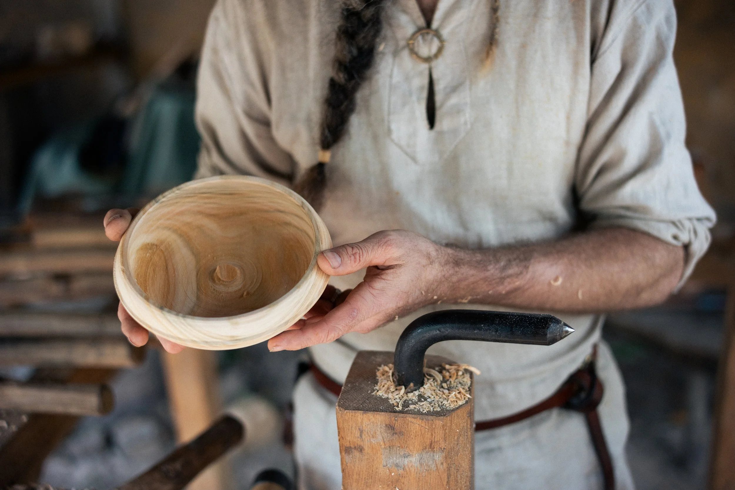A person holding a wooden bowl in a woodworking shop, with a chisel and wood shavings on a work surface.
