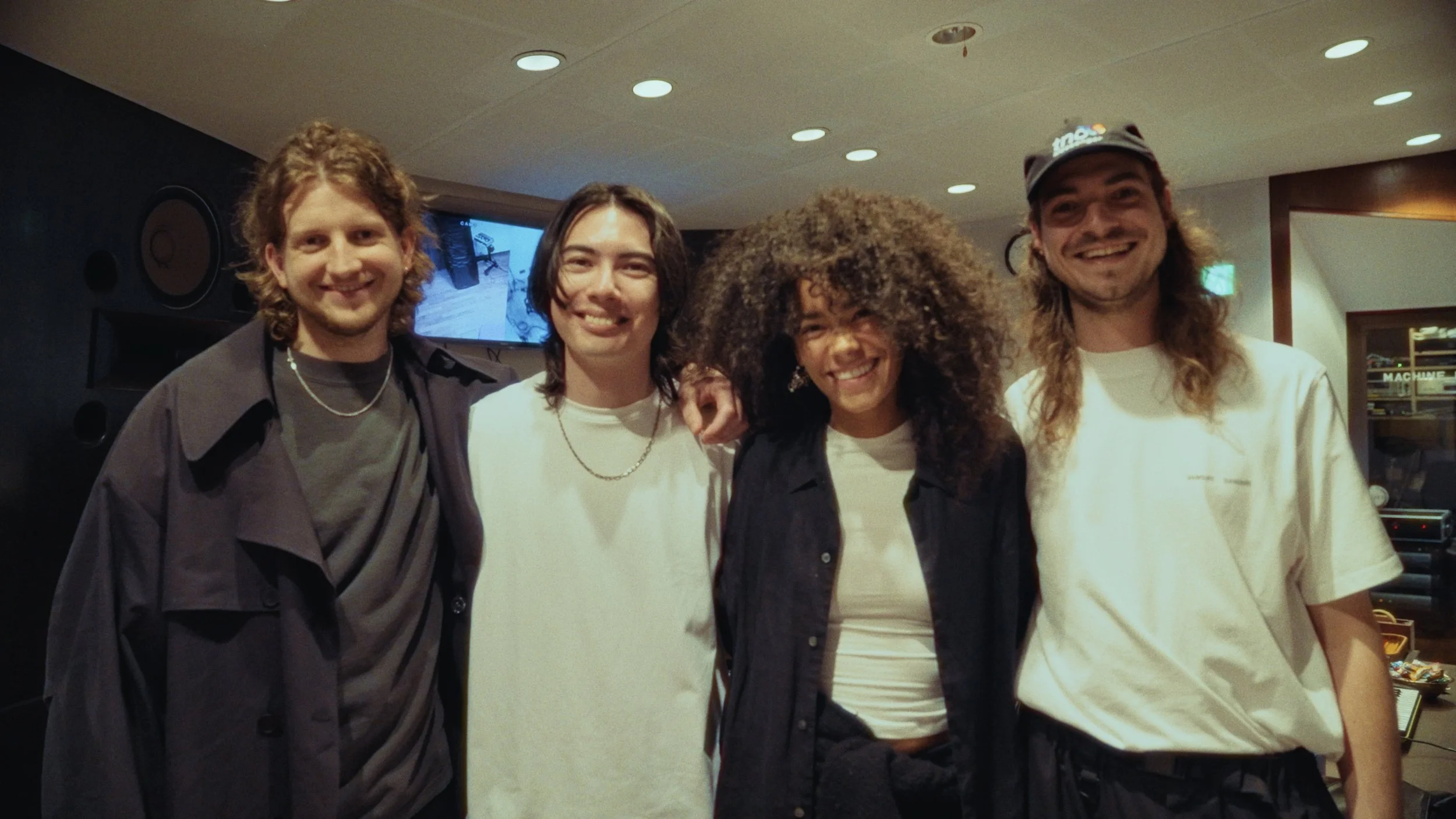 Group of five young people standing together indoors, smiling at the camera.
