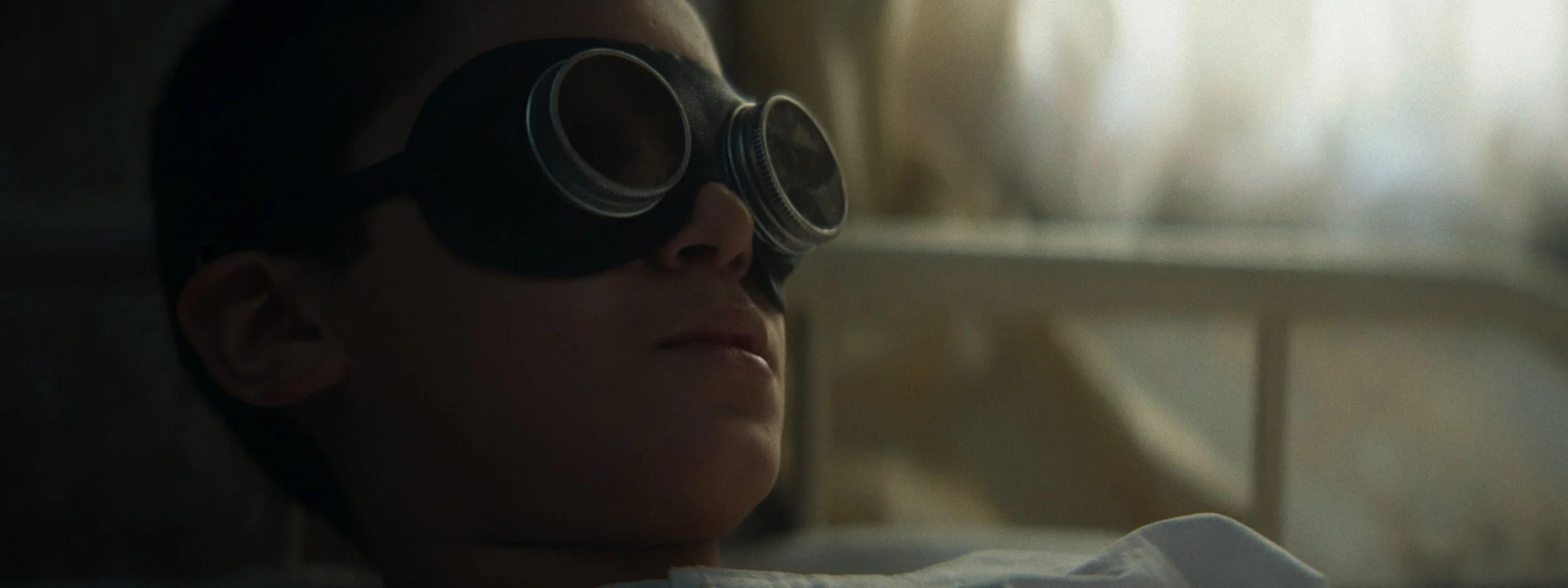 A person wearing protective goggles lying in a hospital bed with a relaxed expression.