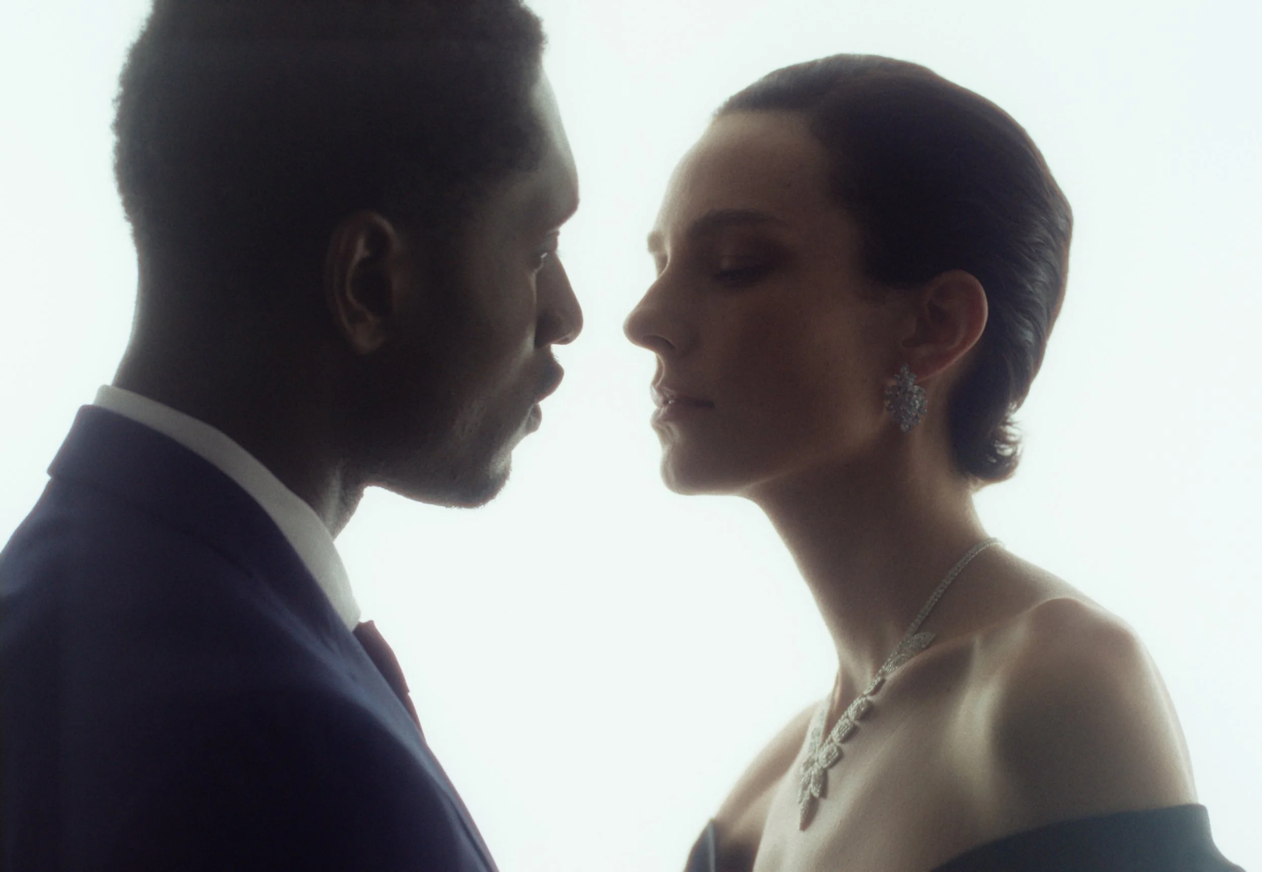 A man and woman face each other closely, appearing to be about to kiss, with a bright background.