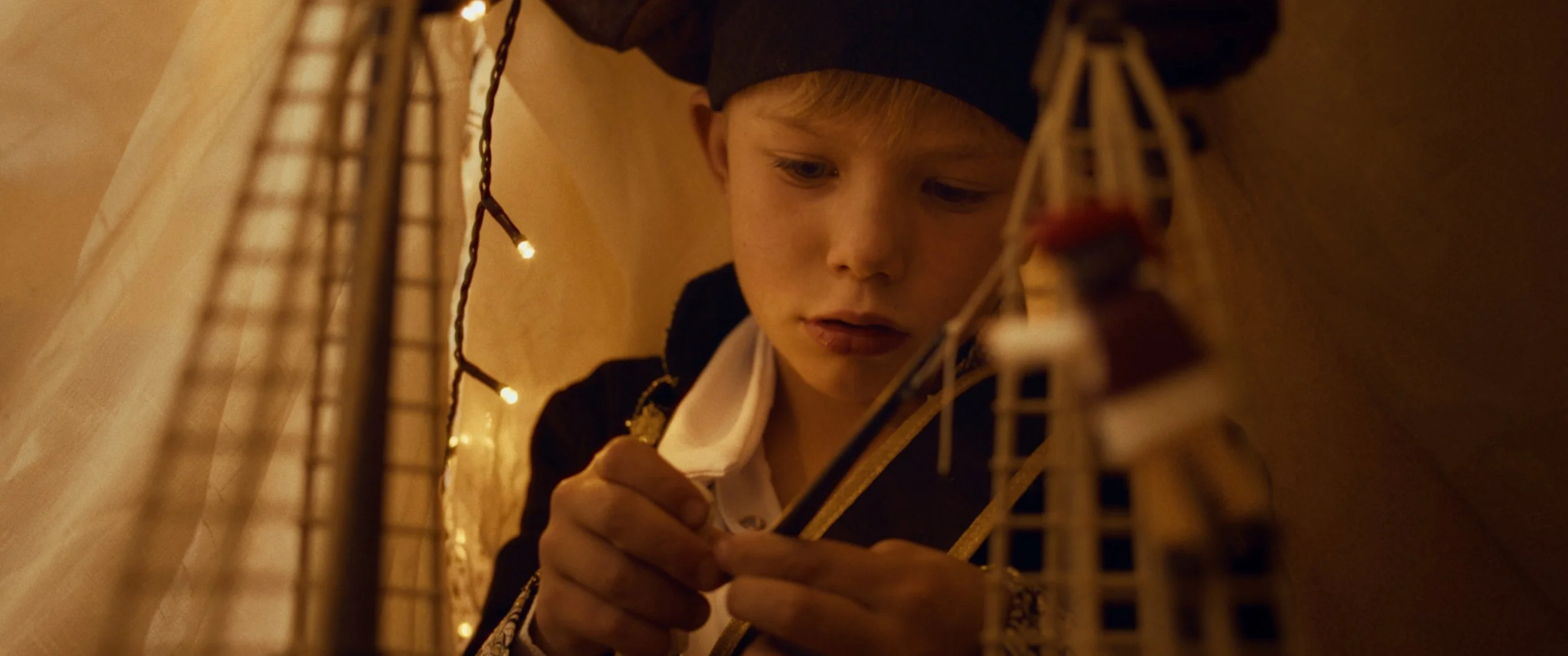 A young boy dressed as a prince, wearing a crown and a pirate costume, is carefully working on a model of the Eiffel Tower, surrounded by warm, soft lighting.