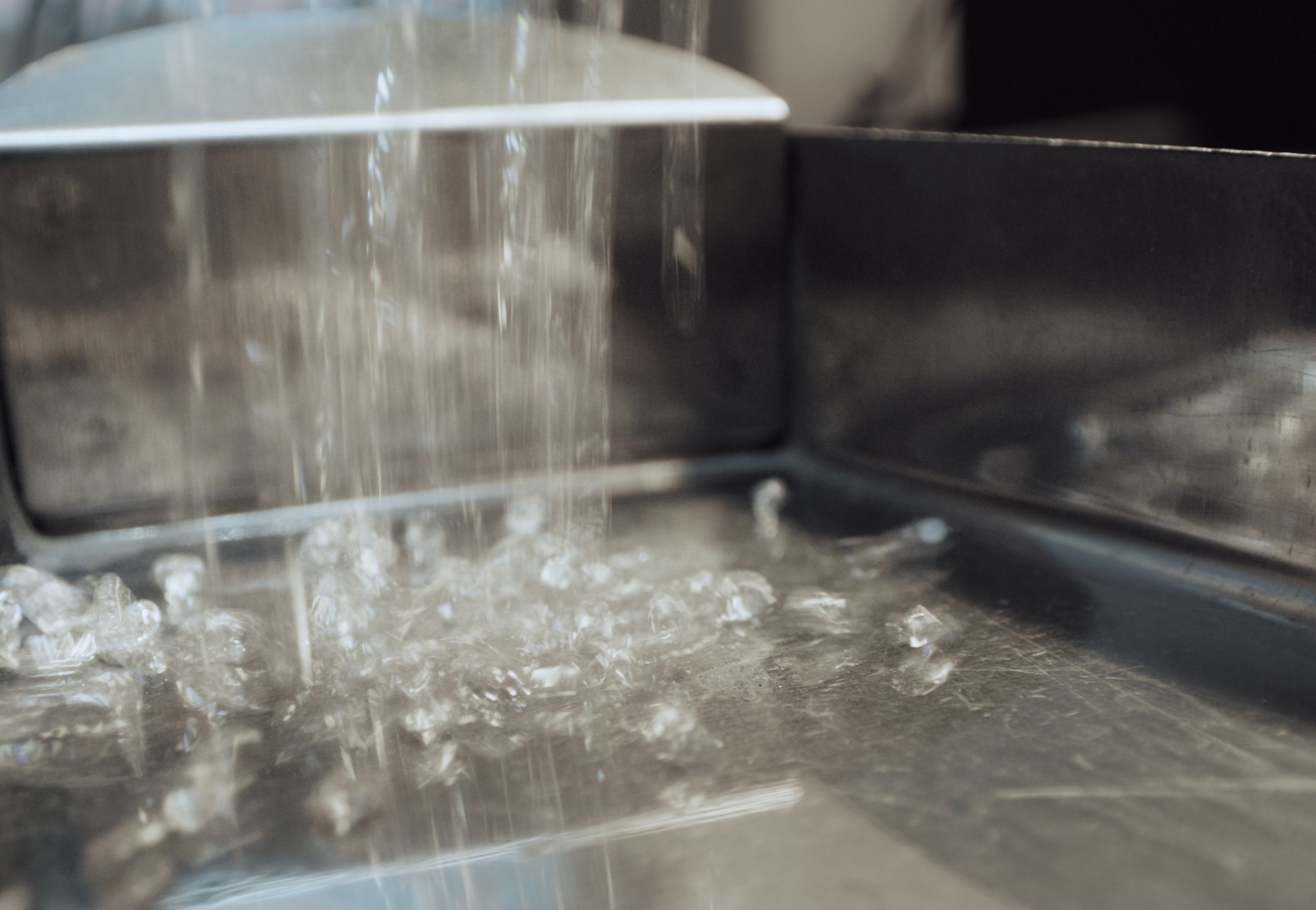 Close-up of a stainless steel machine with water pouring down and ice below, likely a commercial ice maker or water dispenser.