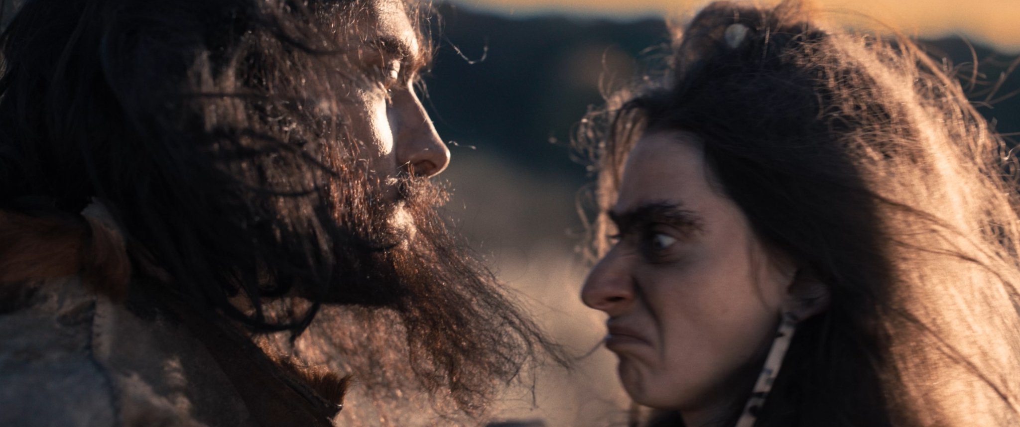 Two women with intense expressions face each other very closely, with their foreheads touching, in a dramatic scene set outdoors, possibly at sunset.