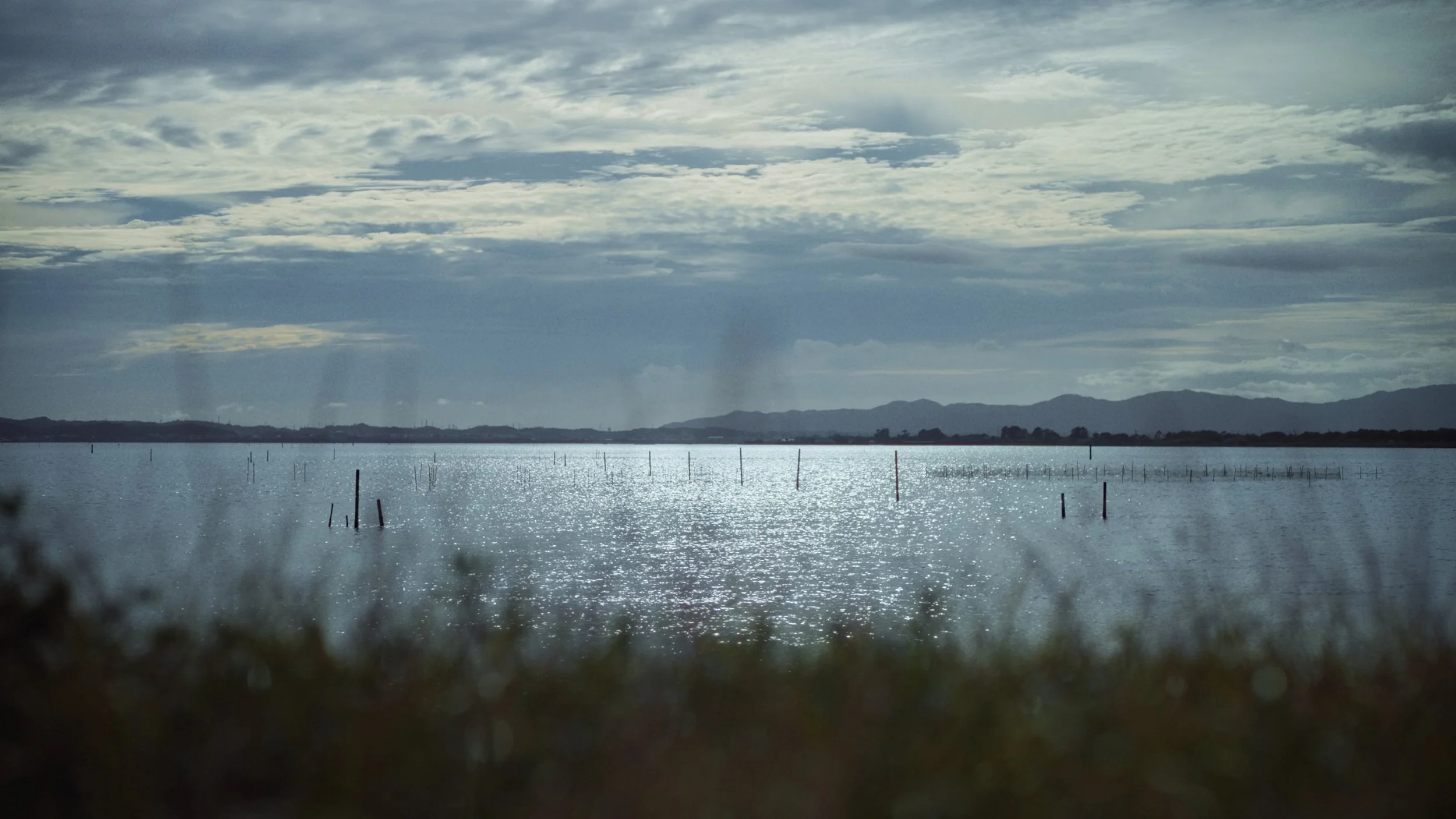 Reflective water body with distant hills under a cloudy sky.
