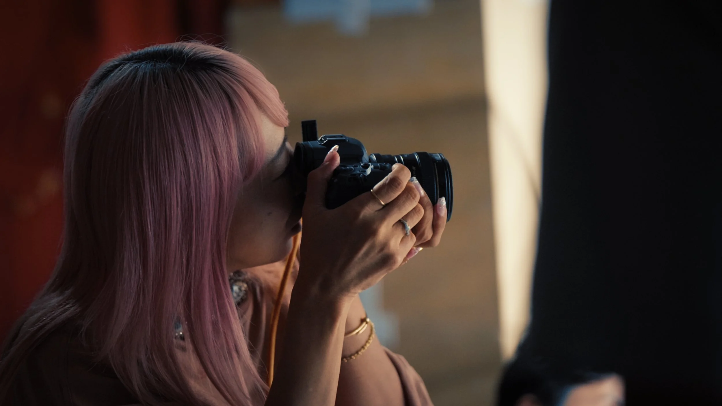 A woman with pink hair taking a photo with a camera.