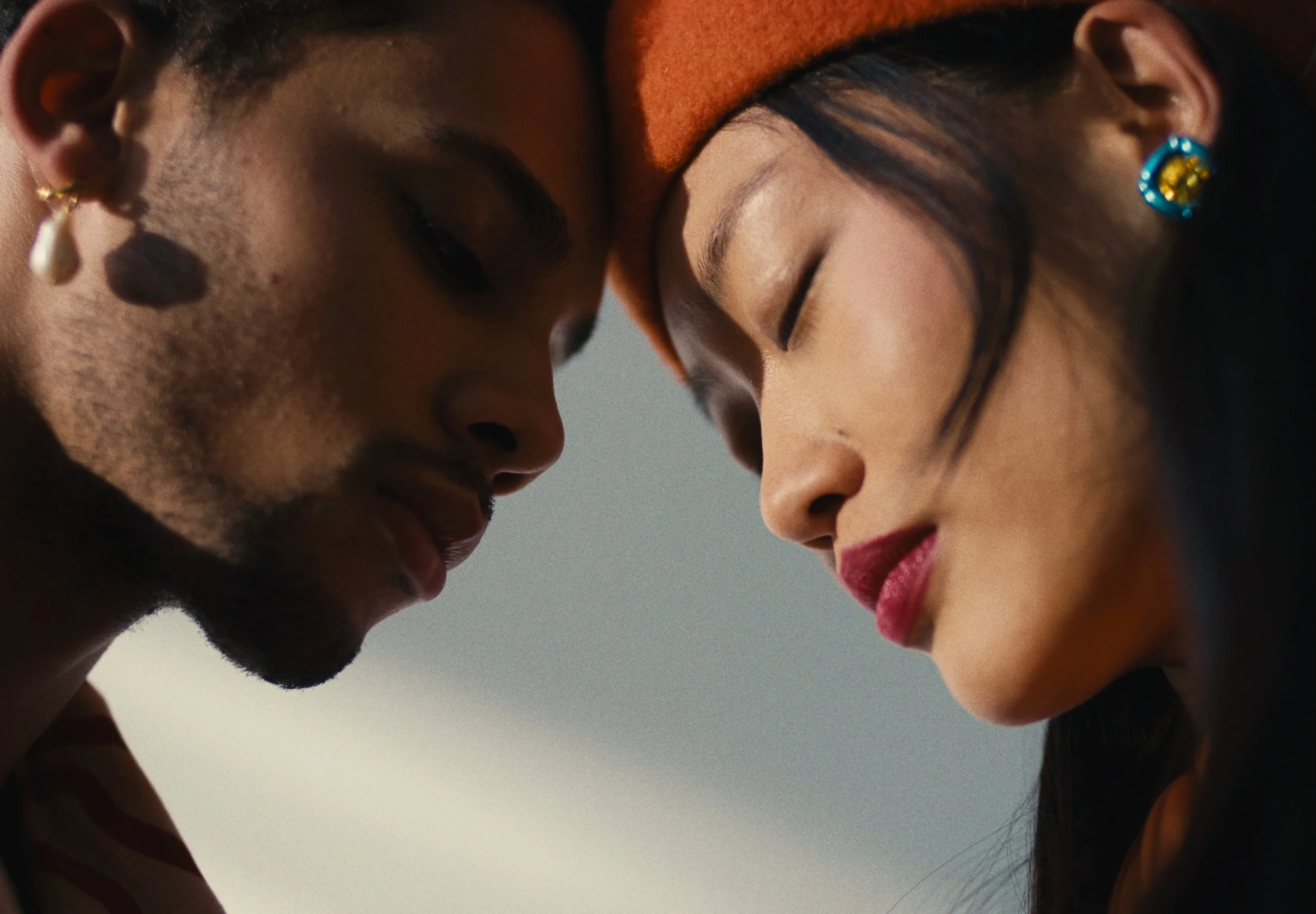 Close-up of a young man and woman with their foreheads touching, eyes closed, and intimate expression.
