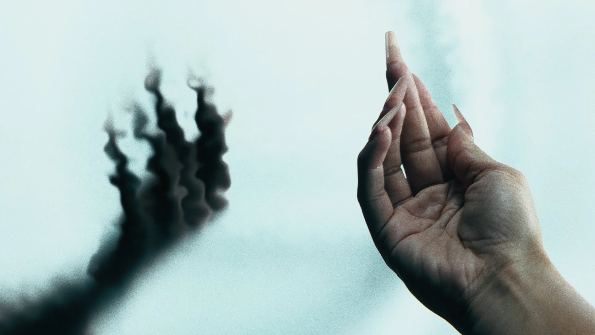 Person's hand with long, manicured nails forming a clay gesture, casting a blurred shadow on the wall.