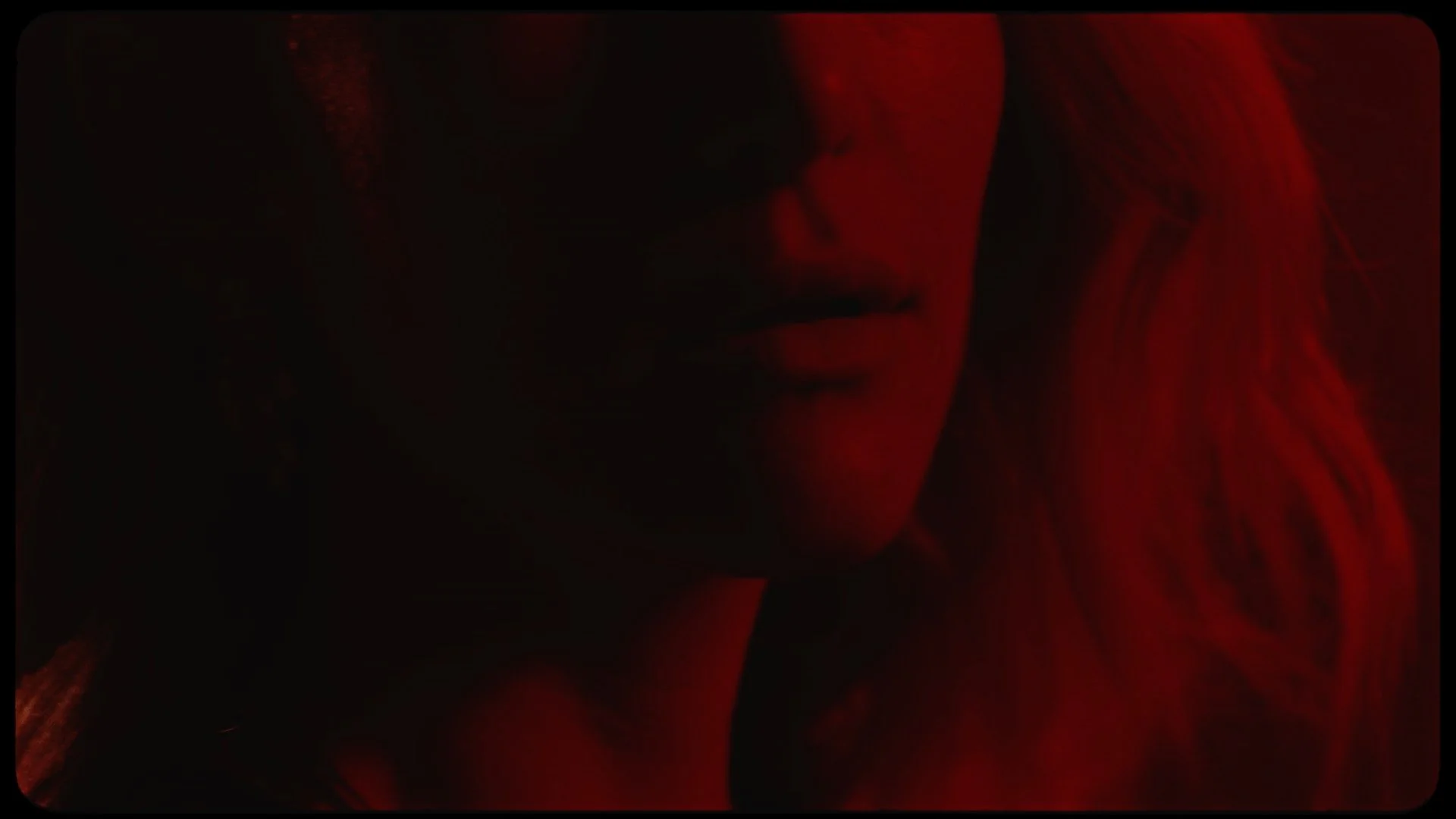 Close-up of a woman's face partially illuminated by red light in a dark setting.