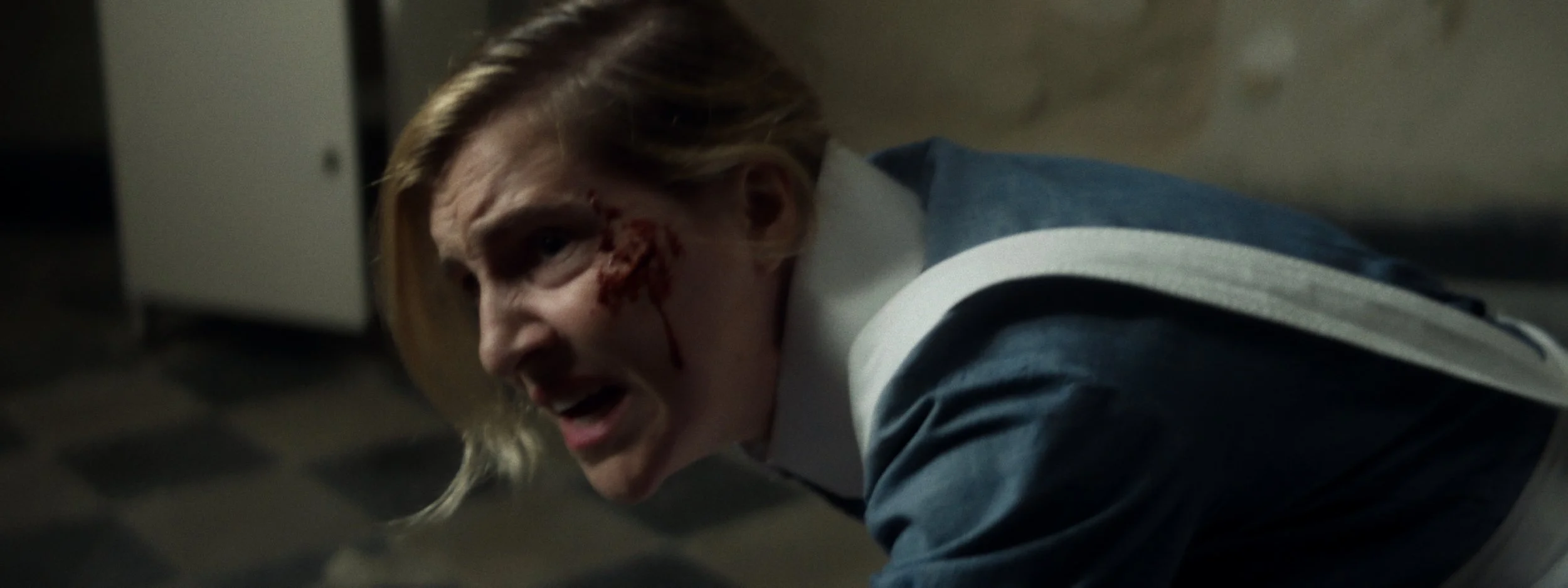 A woman with blood on her face lying on the floor, appearing to be injured.