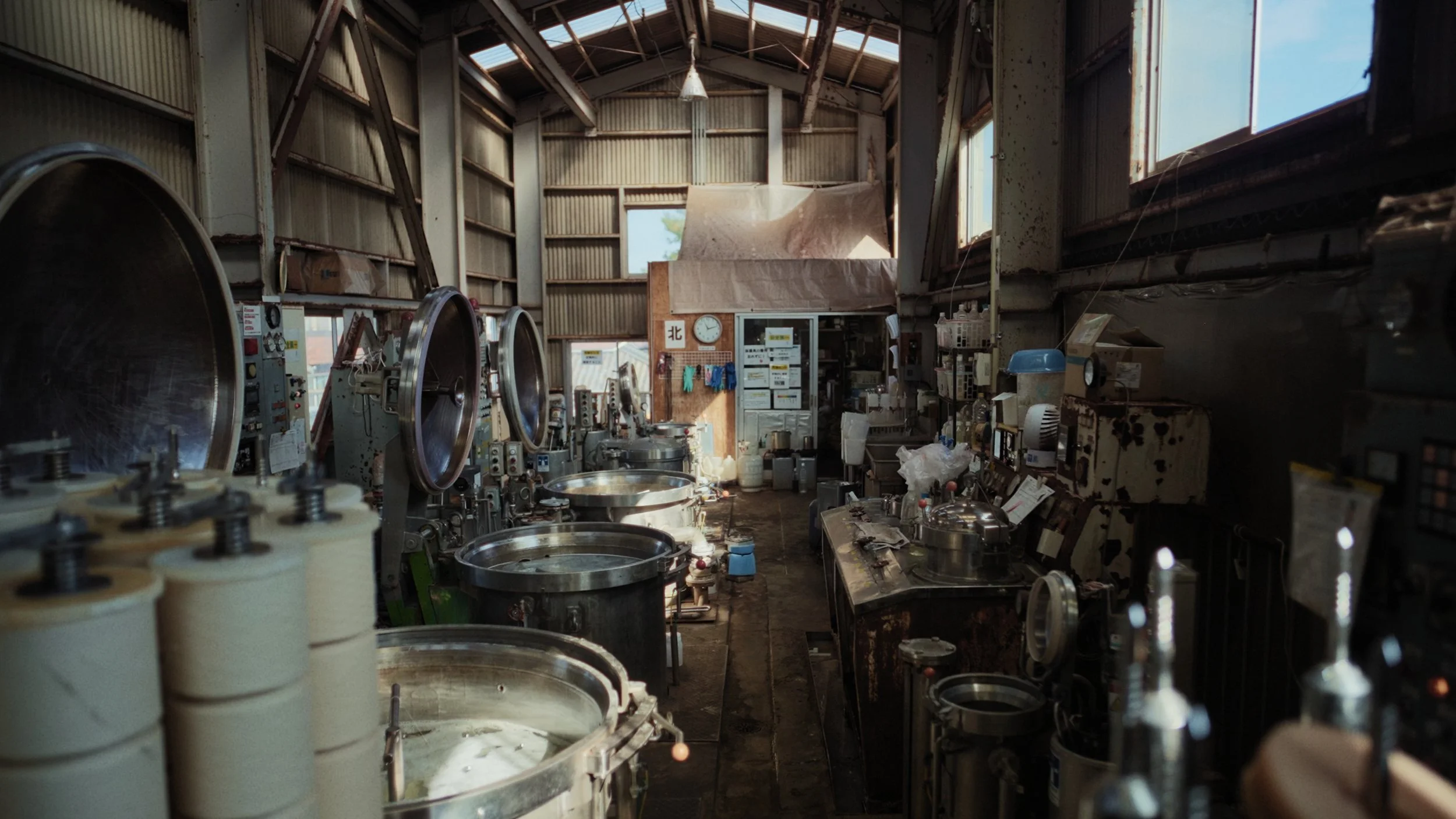 Interior of a laundry facility with washing machines, driers, and various supplies, illuminated by natural light through windows.