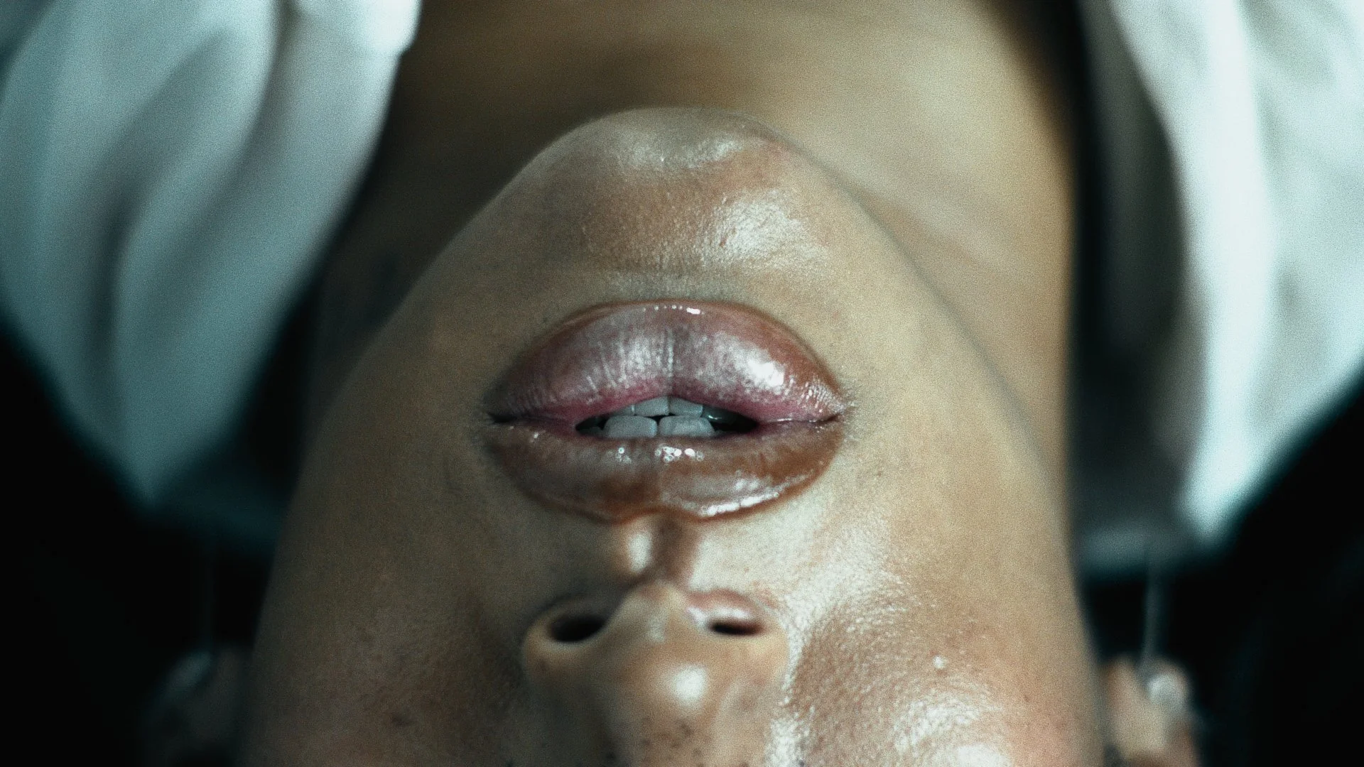 Close-up view of a person's face upside down with lips slightly parted, showing teeth, and wearing glossy lipstick.