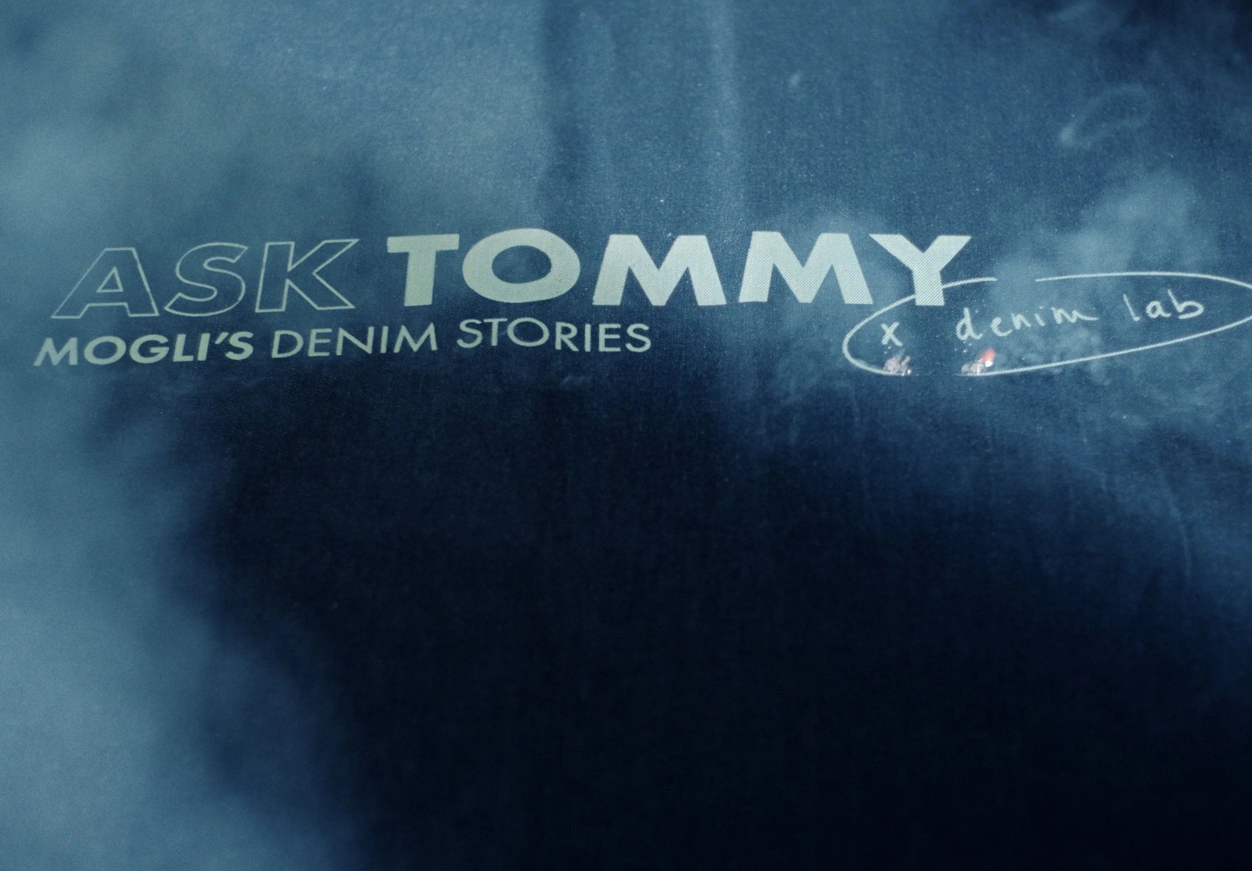 A blue book cover titled 'Ask Tommy: Mogli's Denim Stories' with handwritten notes on the side.