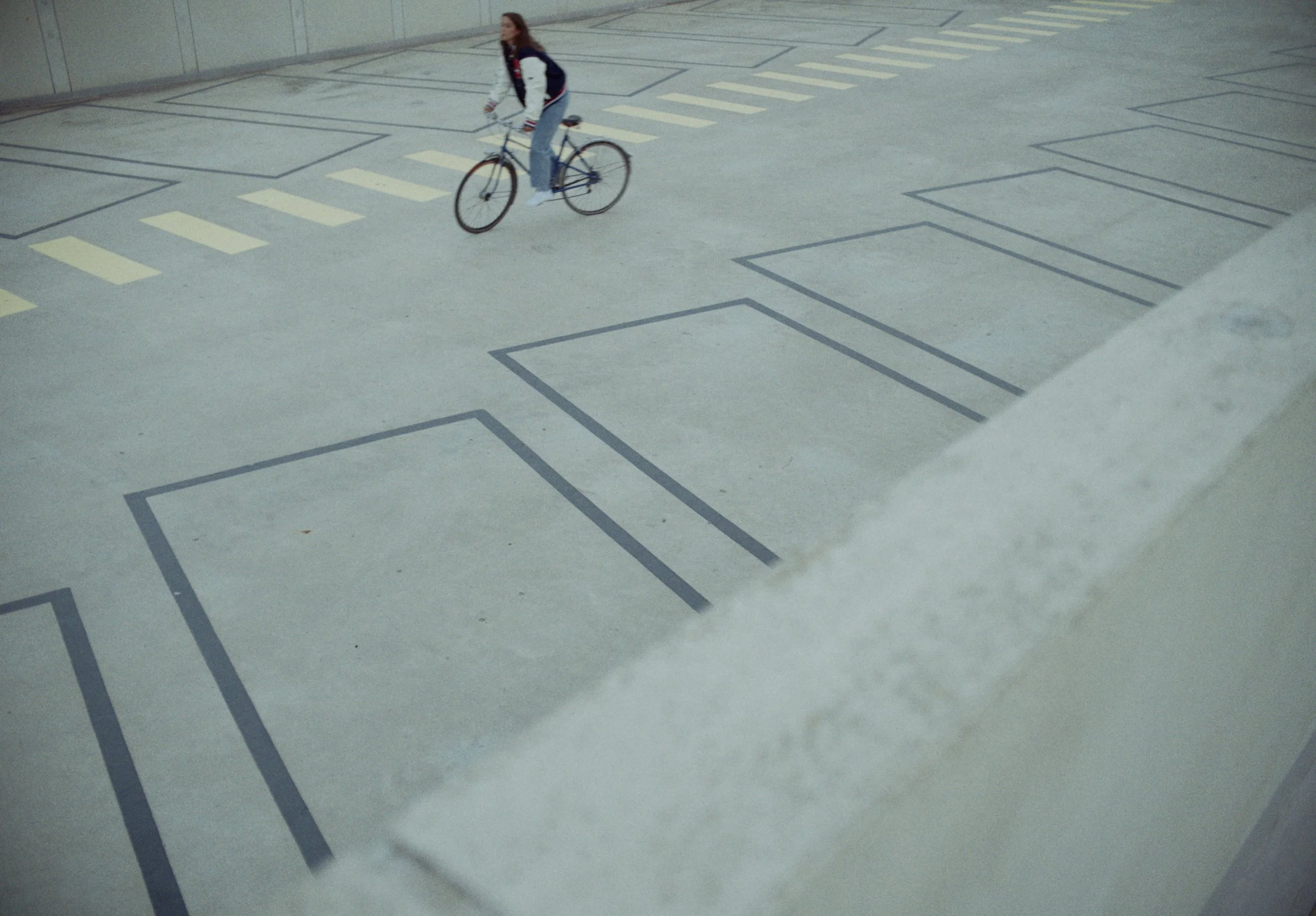 A woman riding a bicycle on a paved area with painted outlines and markings.