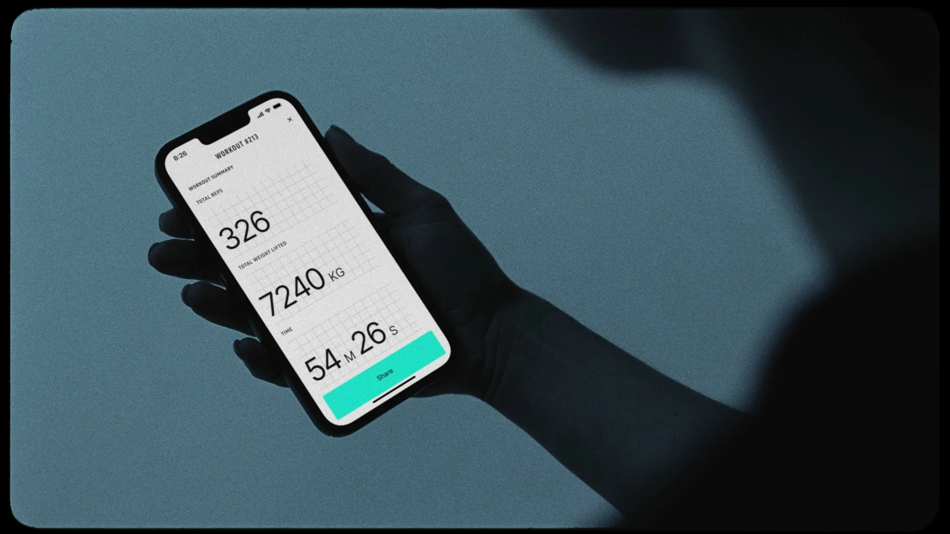 A person wearing black gloves holding a smartphone displaying a workout summary, including total reps (326), total weight lifted (7240 kg), and time (54 minutes and 26 seconds).