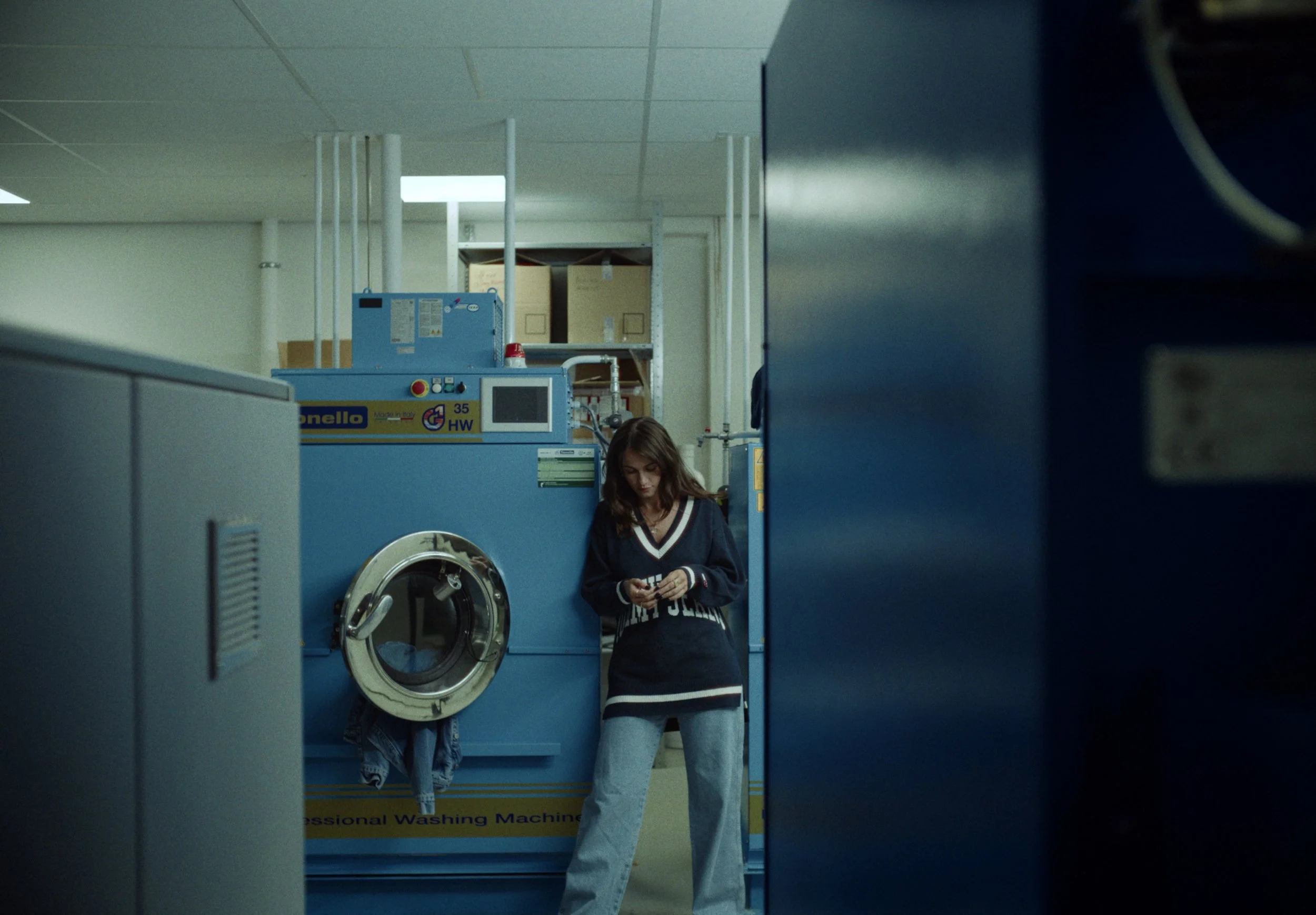 A woman standing next to a blue industrial washing machine in a laundry room, with her head and shoulders visible as she looks down.