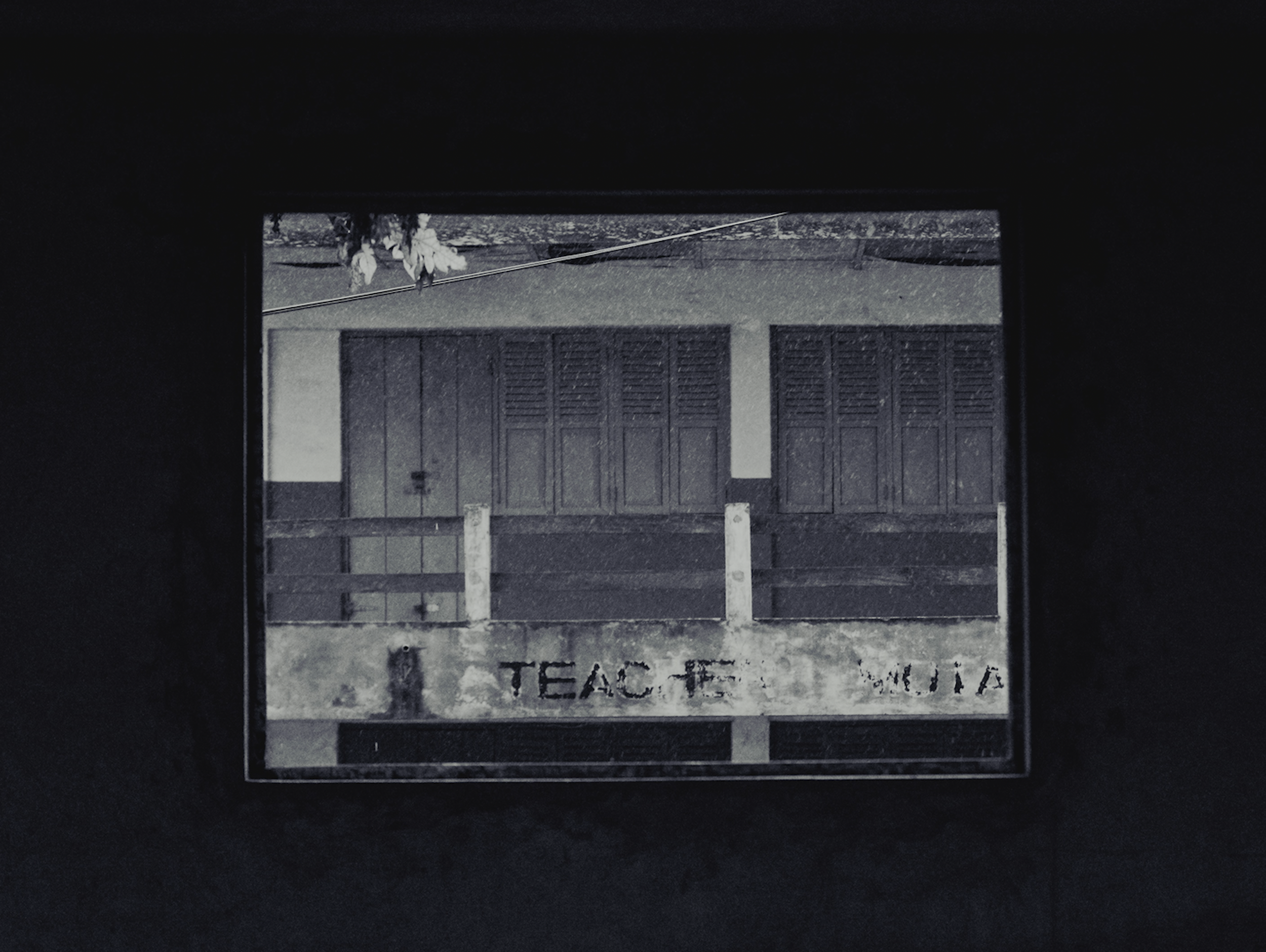A dark photograph of a school gate with wooden doors and a sign that reads "TEACHERS ONLY."