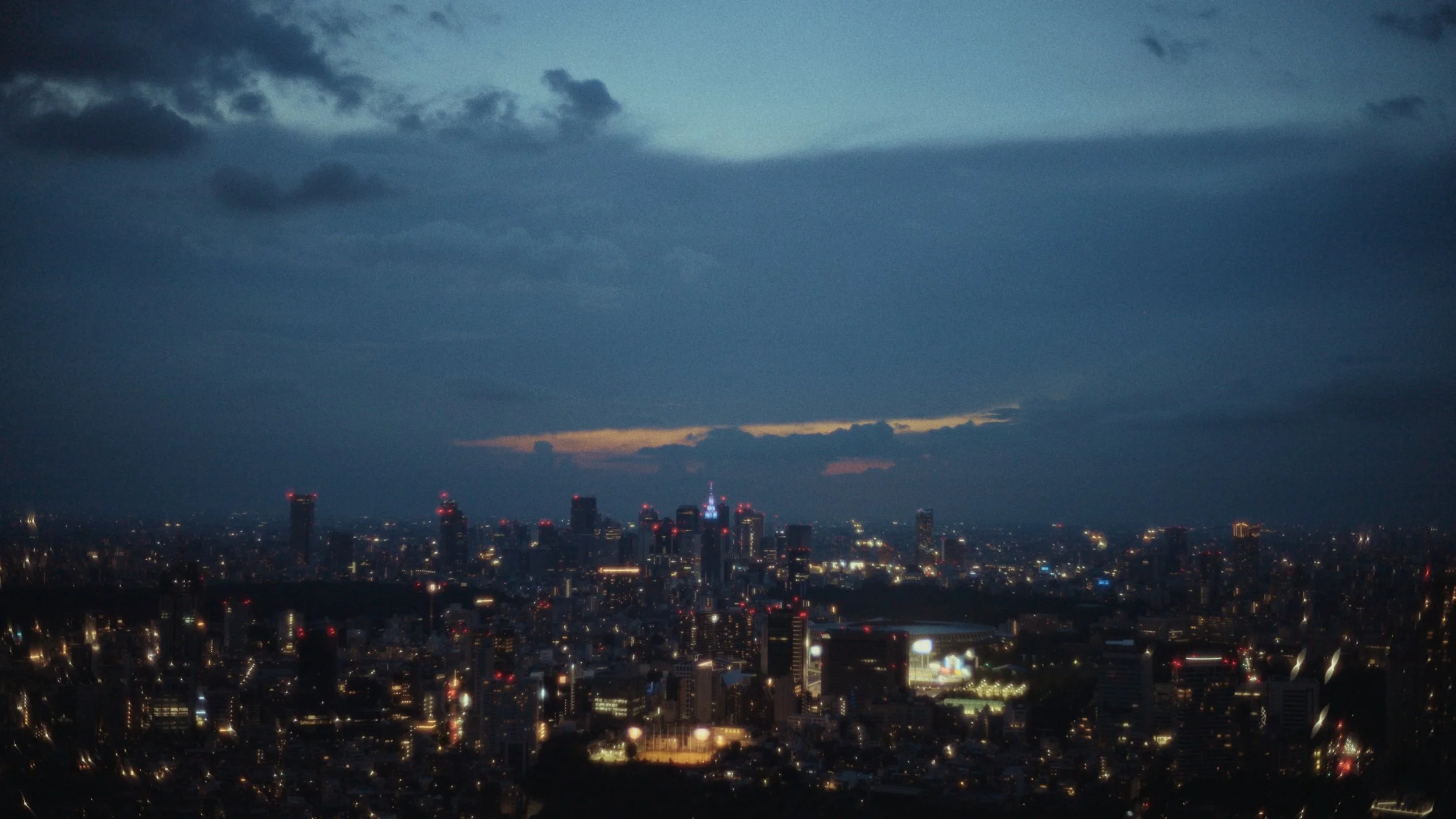City skyline at dusk with illuminated buildings and a cloudy sky.