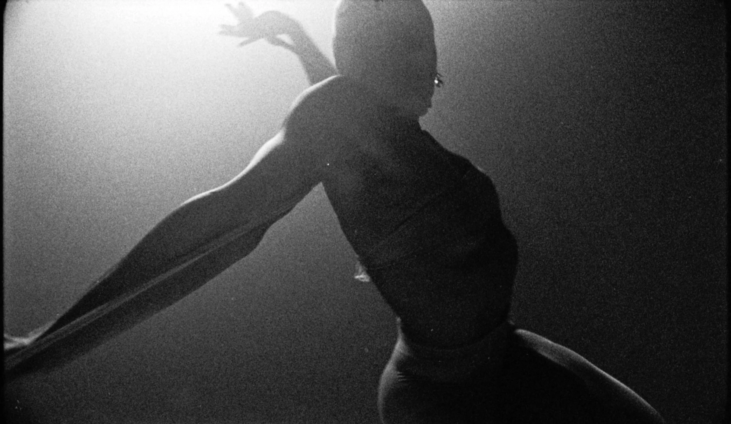 Silhouette of a woman in a dance pose with one arm raised and head tilted back, seen through a window or glass panel with a bright light behind her.
