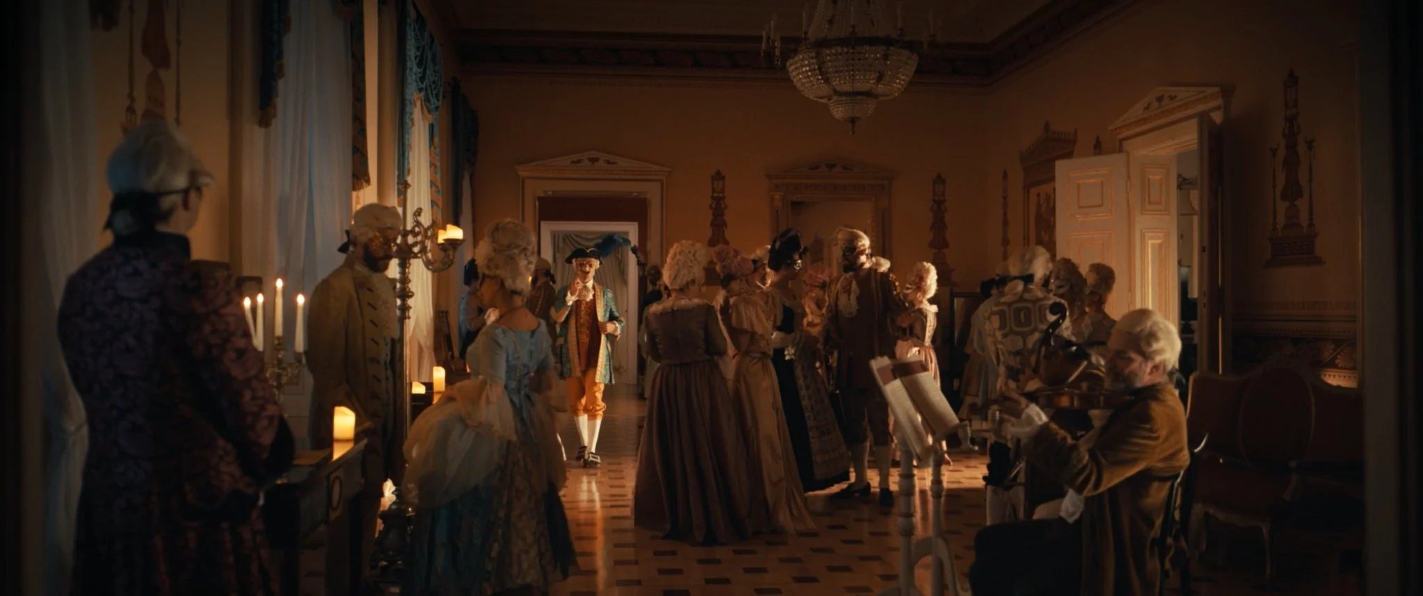 People dressed in 18th-century costumes attending a social gathering in an opulent room with chandeliers and candlelit ambiance.