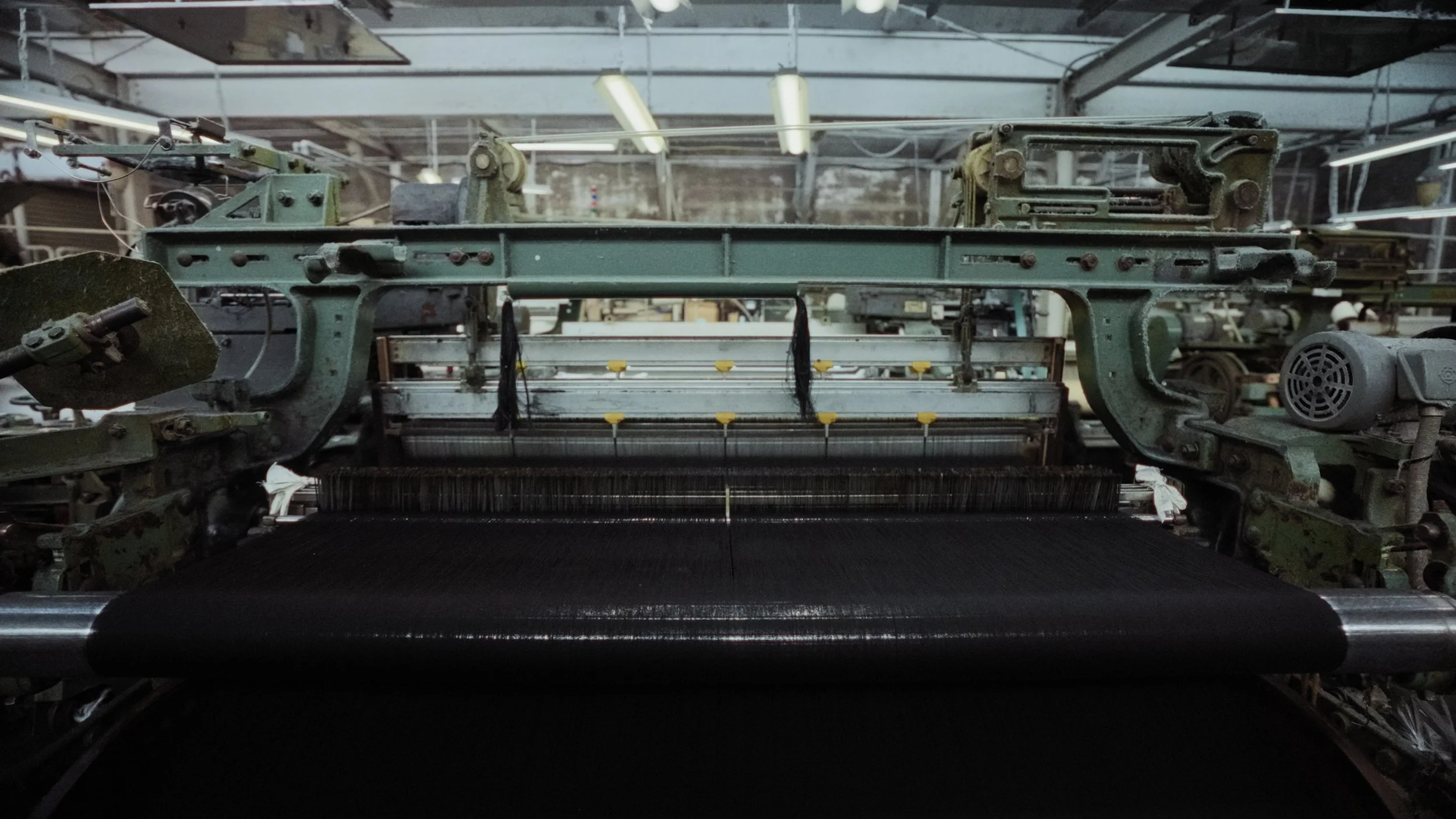 Close-up of a vintage industrial textile weaving machine in a factory with metal parts and rollers.