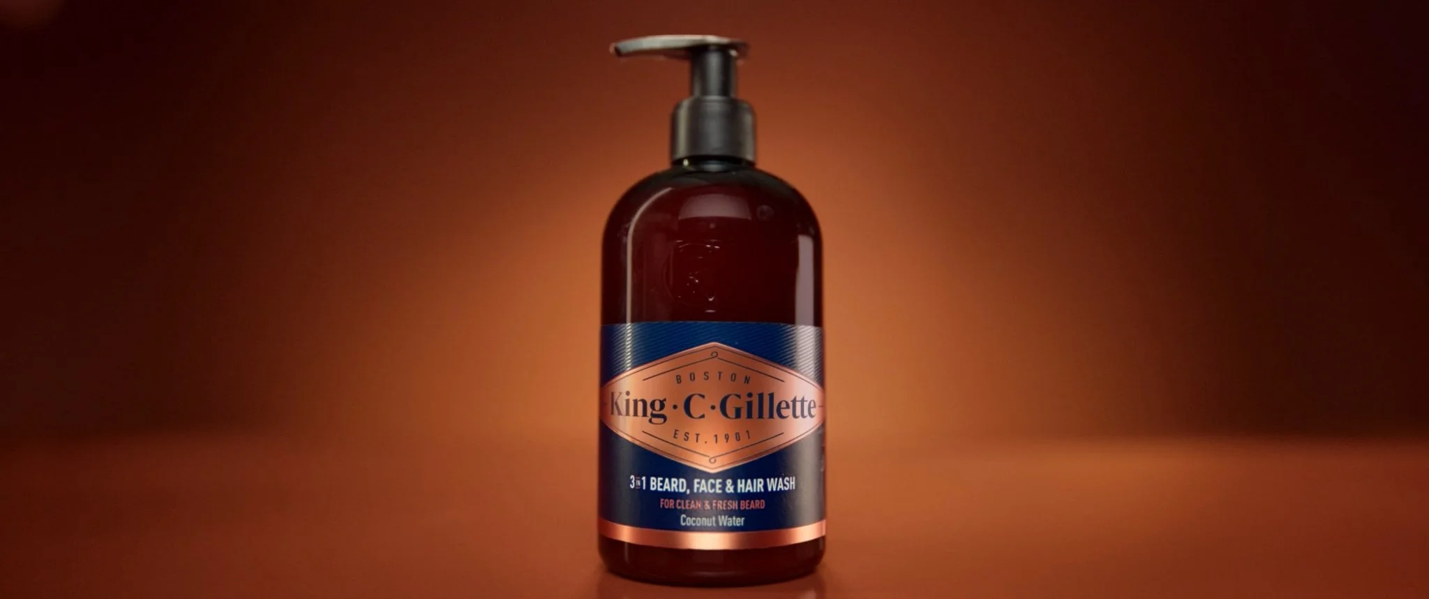 Bottle of King C. Gillette 3-in-1 beard, face, and hair wash with coconut water, placed against a warm brown background.