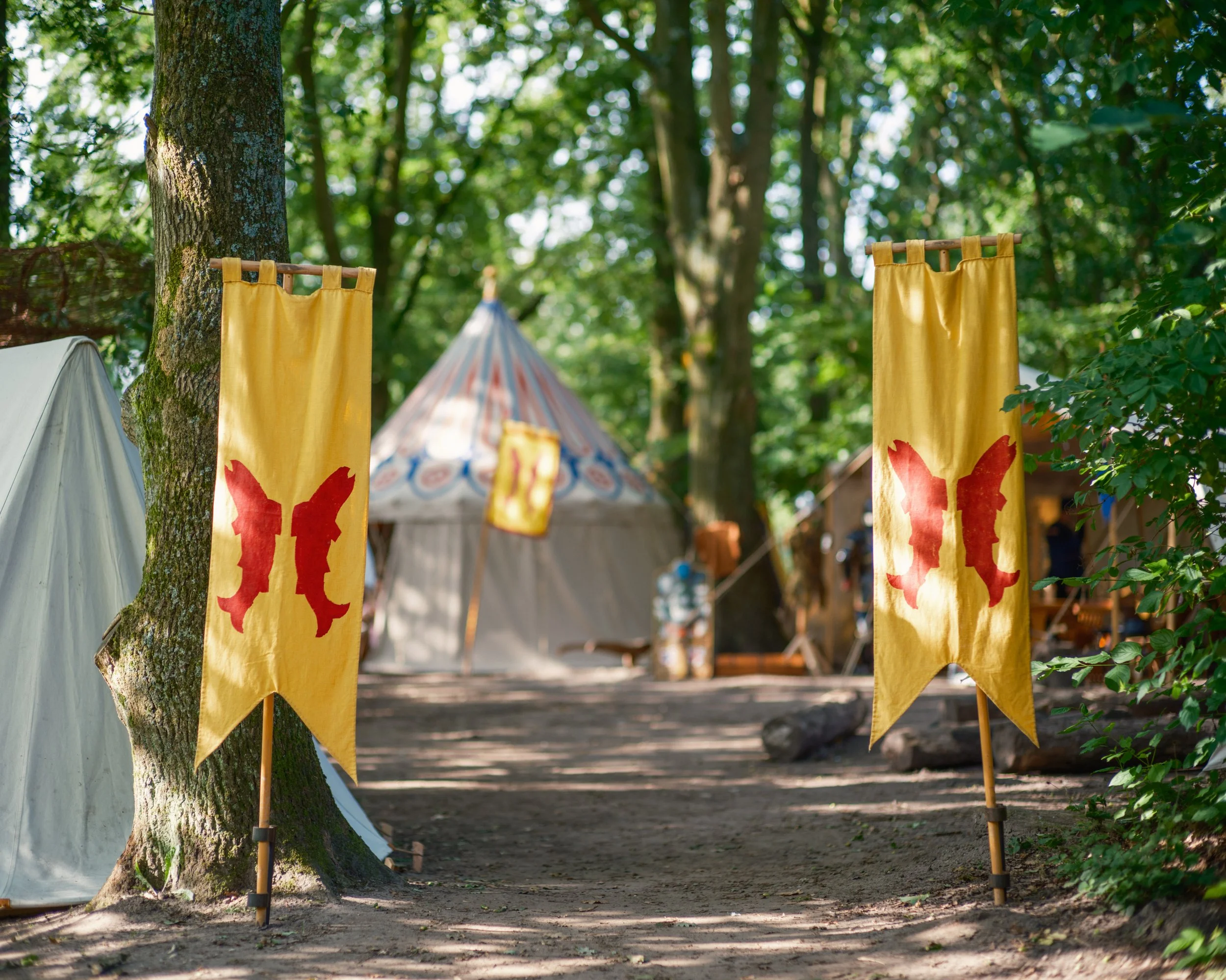 Yellow banners hanging from trees with a red design, set in a forested outdoor area with tents and greenery.