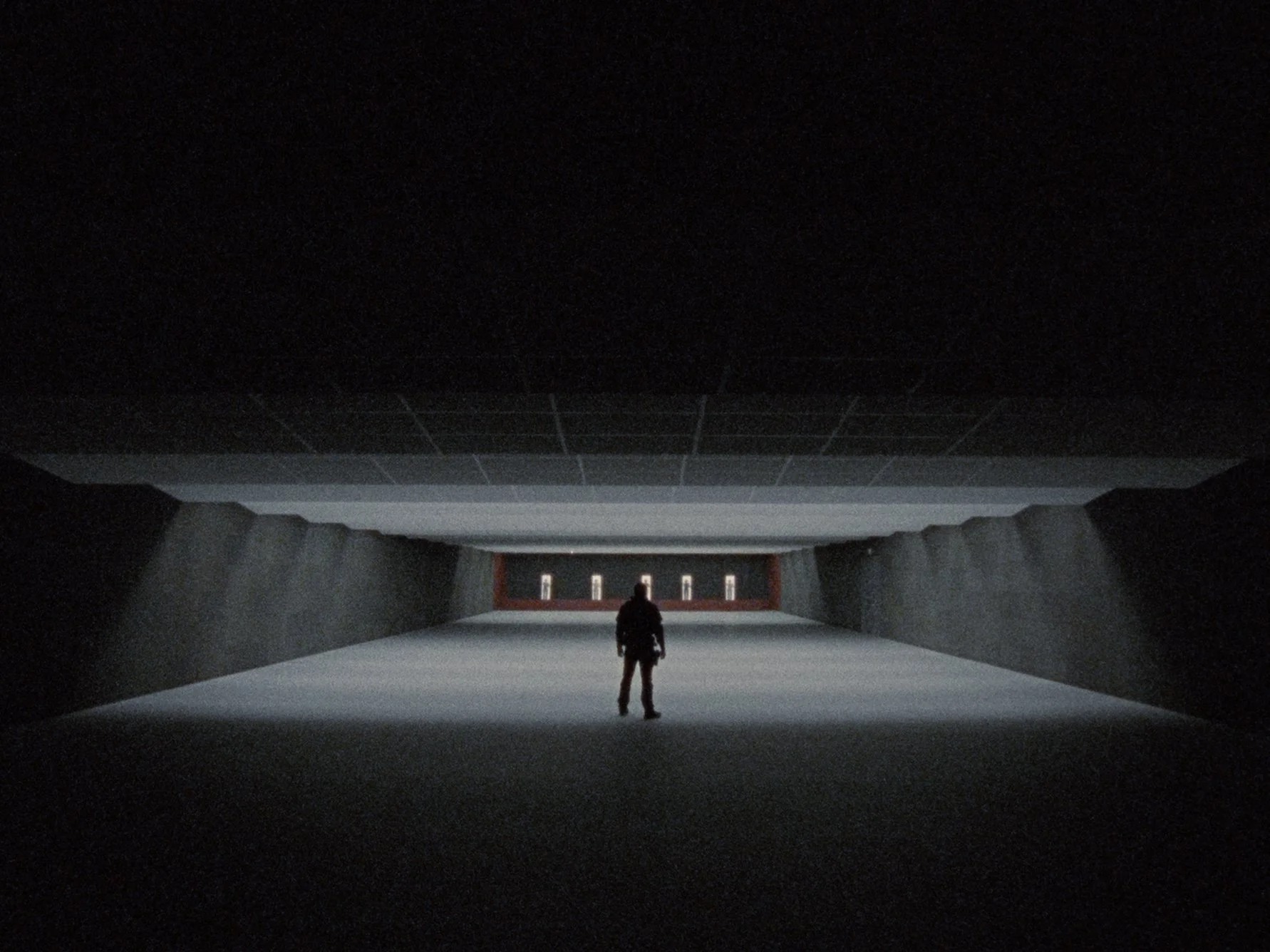 A person standing inside a dark, tunnel-like structure with a brightly lit opening at the far end, showing some small objects or figures in the distance.
