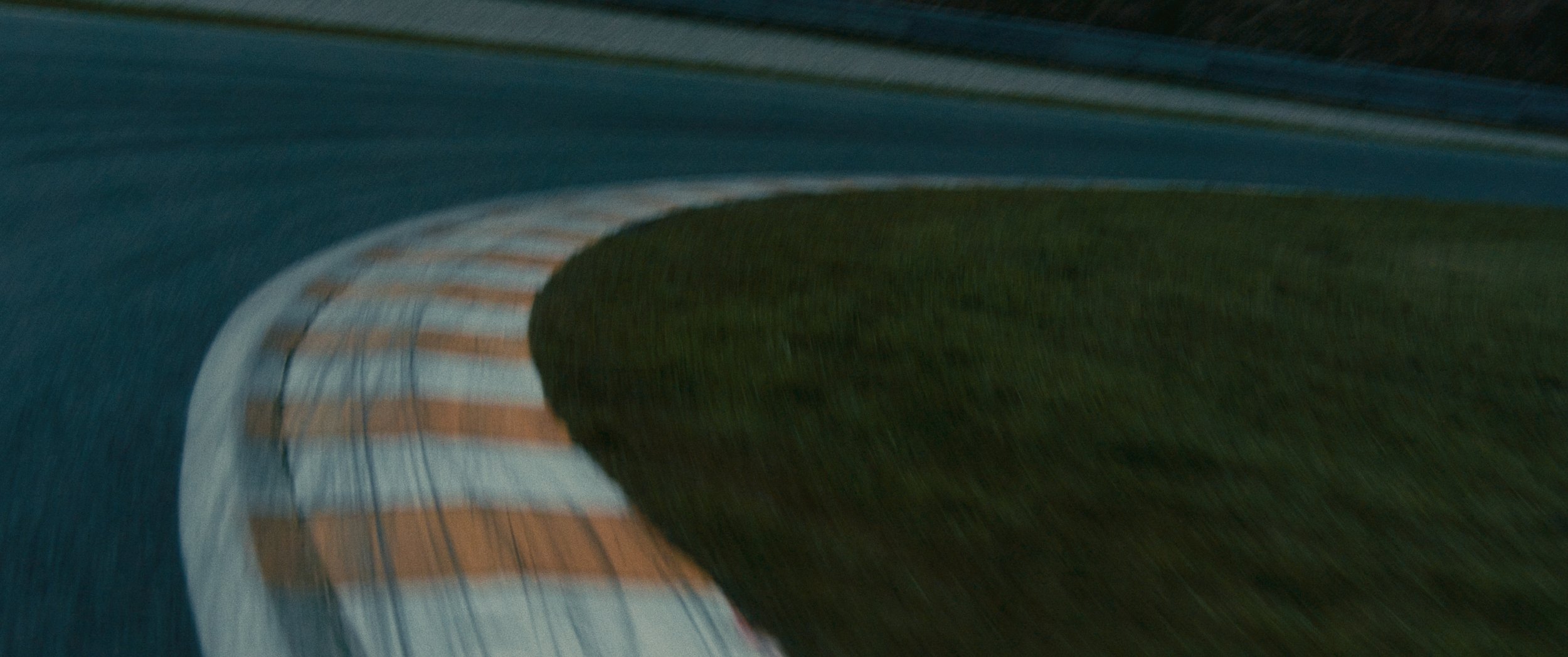 Blurred nighttime photo of a curving racetrack with a grassy area in the center.