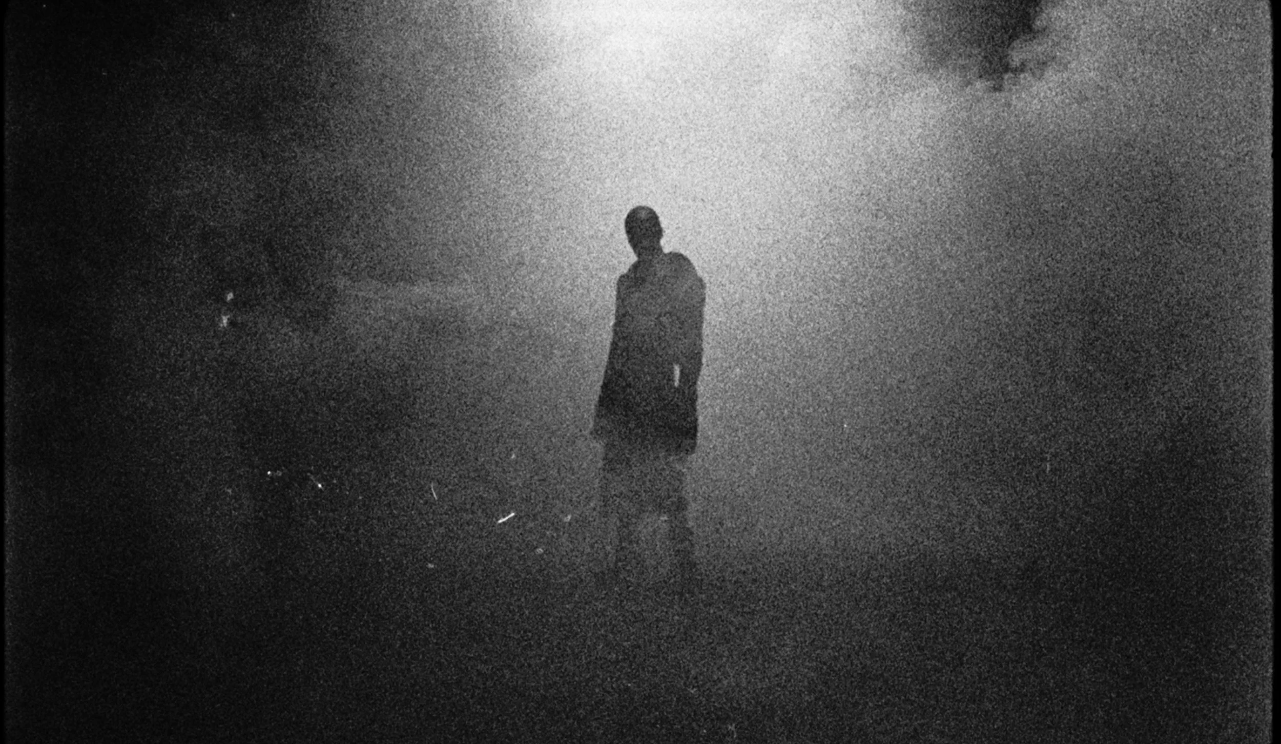 A silhouette of a person standing on a foggy or smoky ground with a cloudy sky in the background.