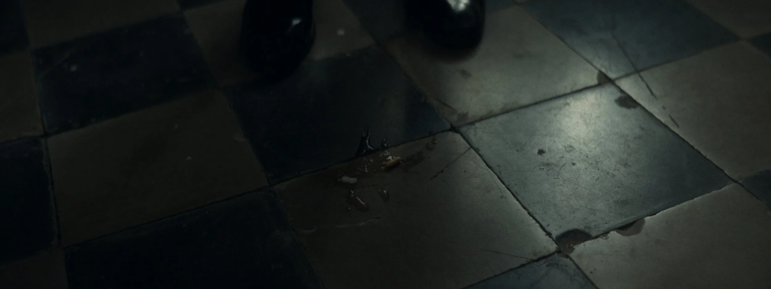 Dark tiled floor with a small group of cigarette butts and a few drops of liquid.