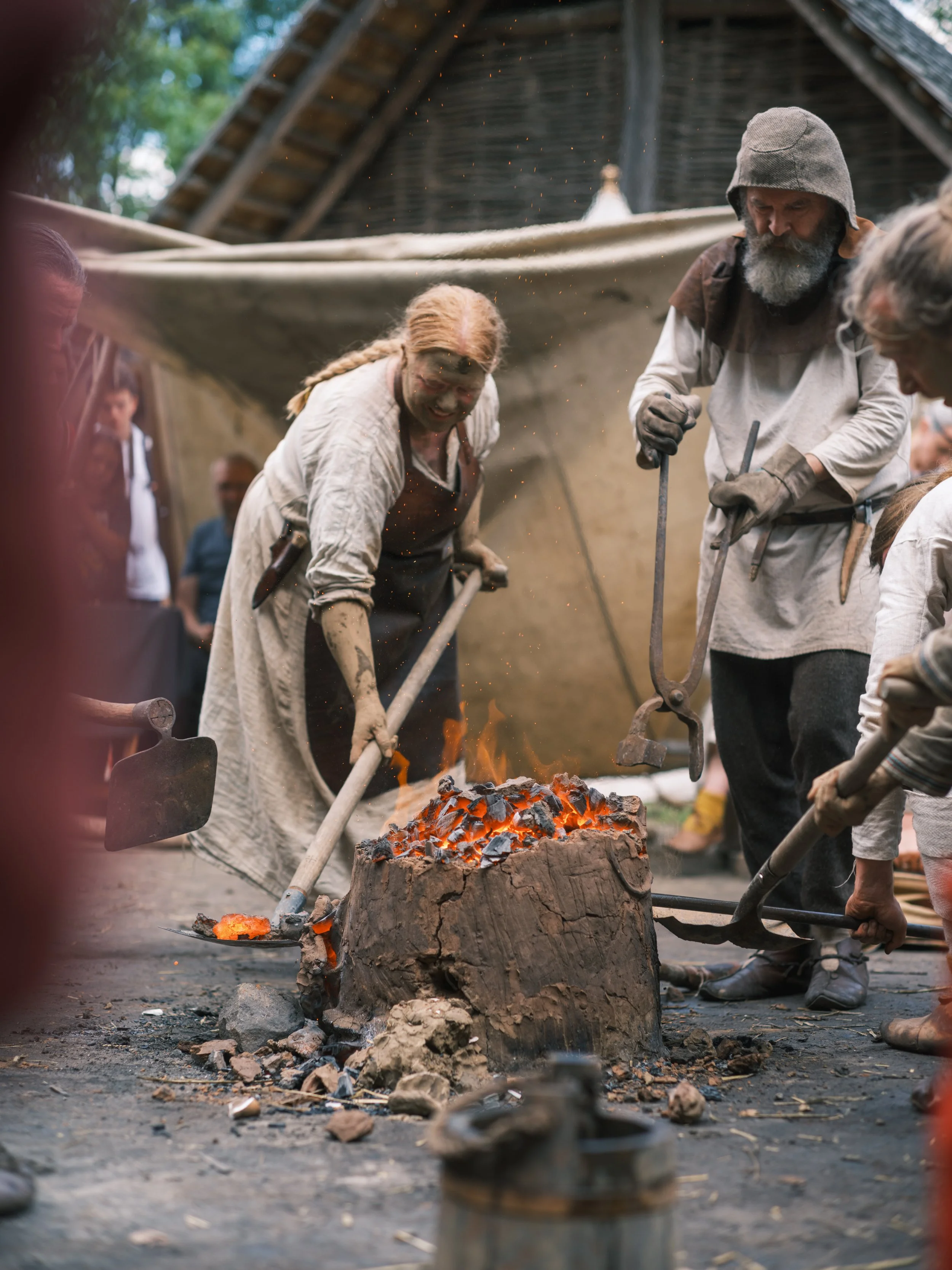 Blacksmiths forge metal on an anvil amidst sparks and hot lava inside a rustic workshop.