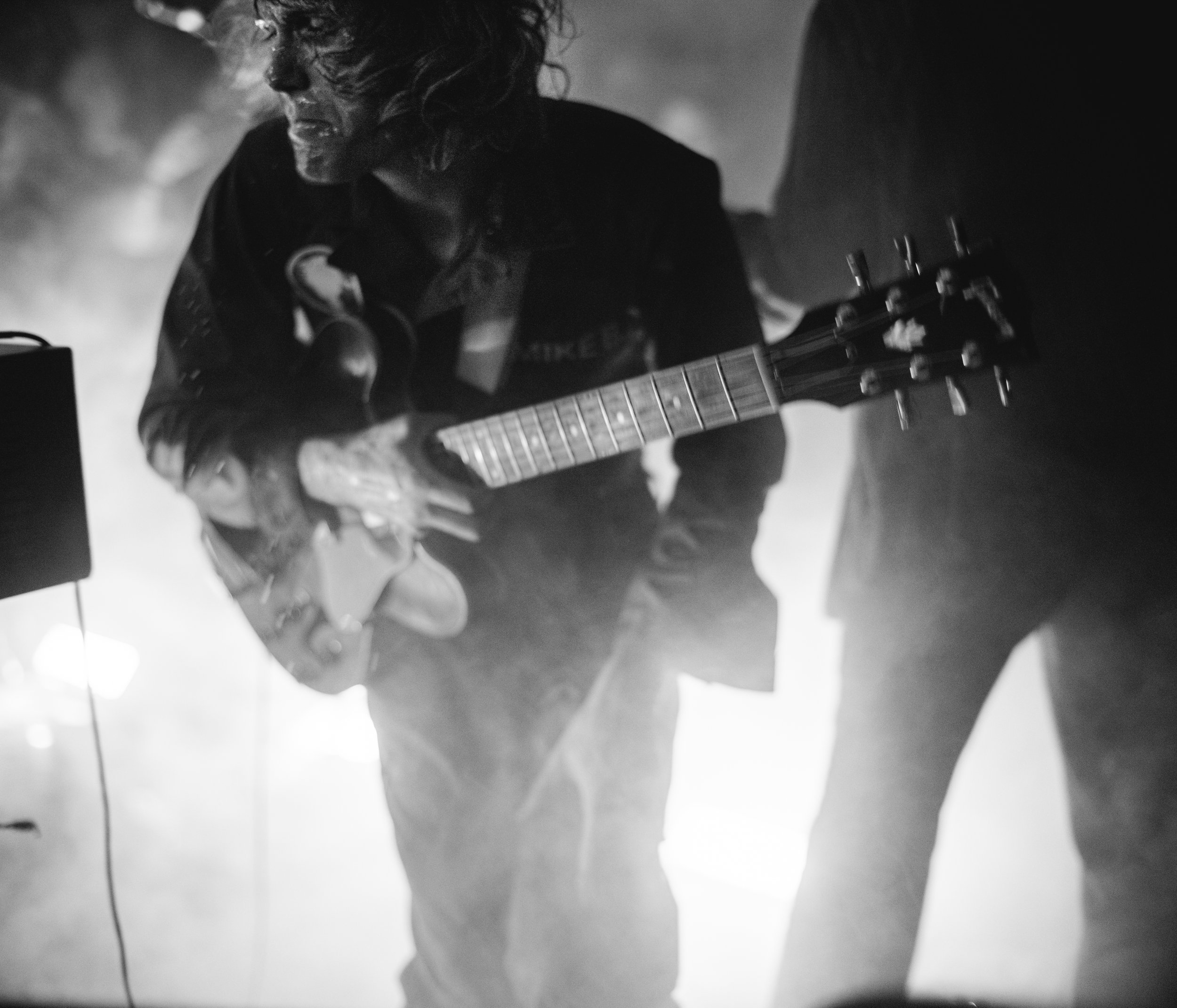 Black and white photo of a woman playing an acoustic guitar in a live performance setting.