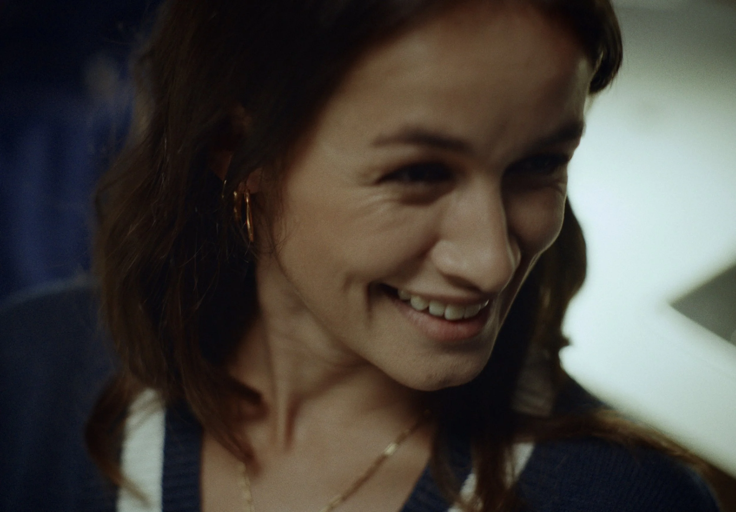 A close-up of a smiling woman with brown hair and gold hoop earrings.