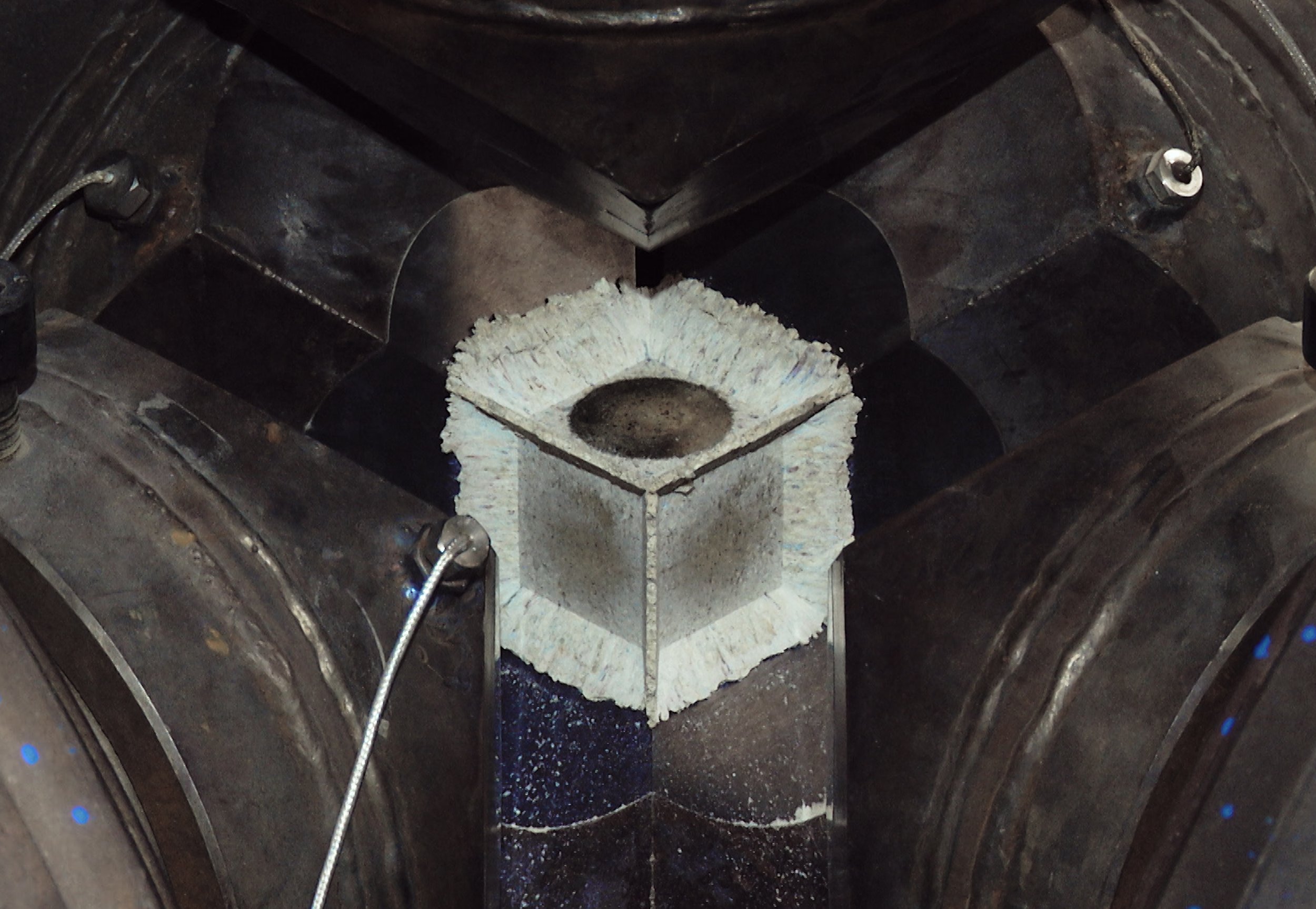 Close-up of a mechanical component with a central metal piece, surrounded by dark parts and bolts, possibly a machine or engine part.
