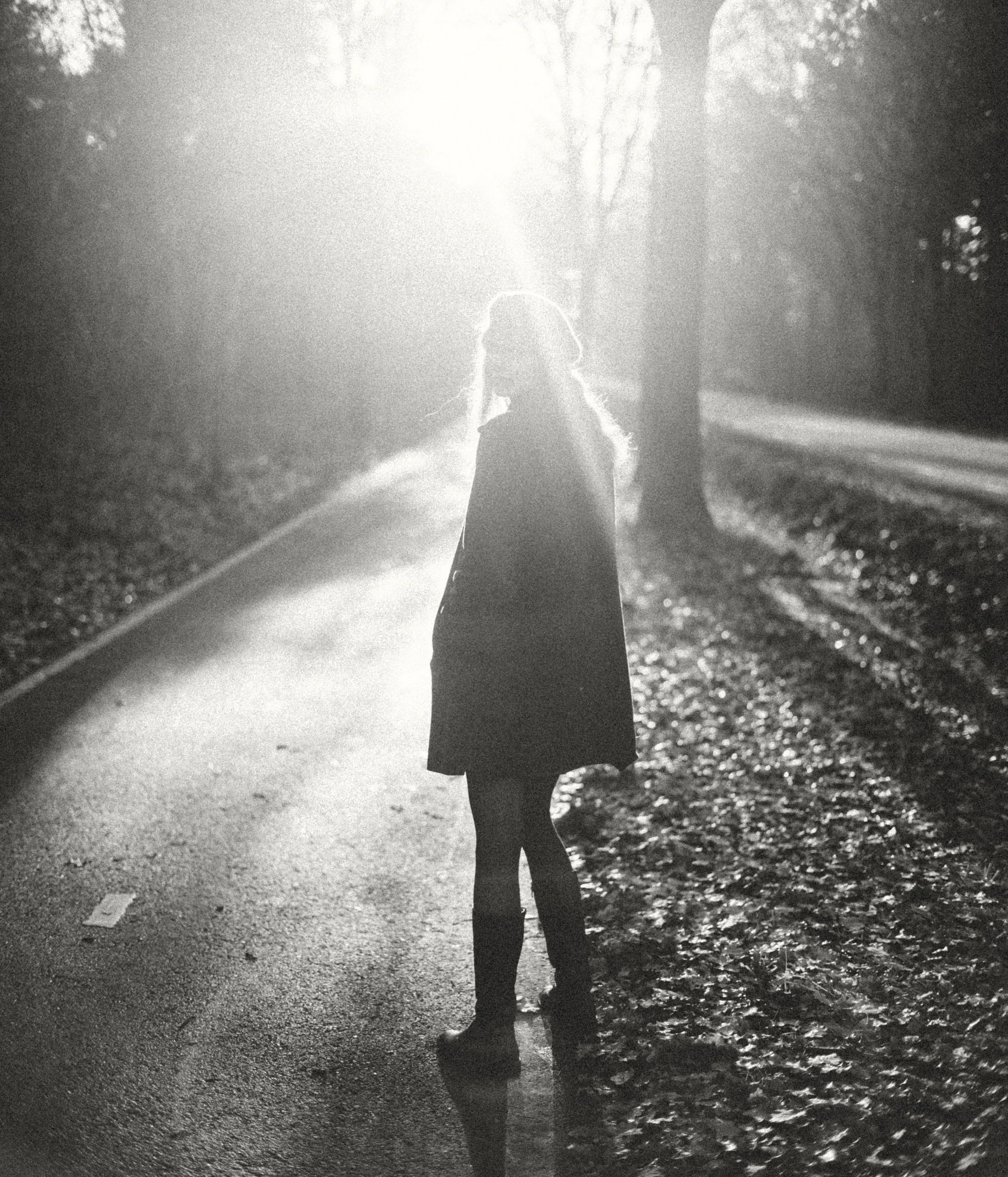A person walking on a road with sunlight shining in the background, captured in black and white.