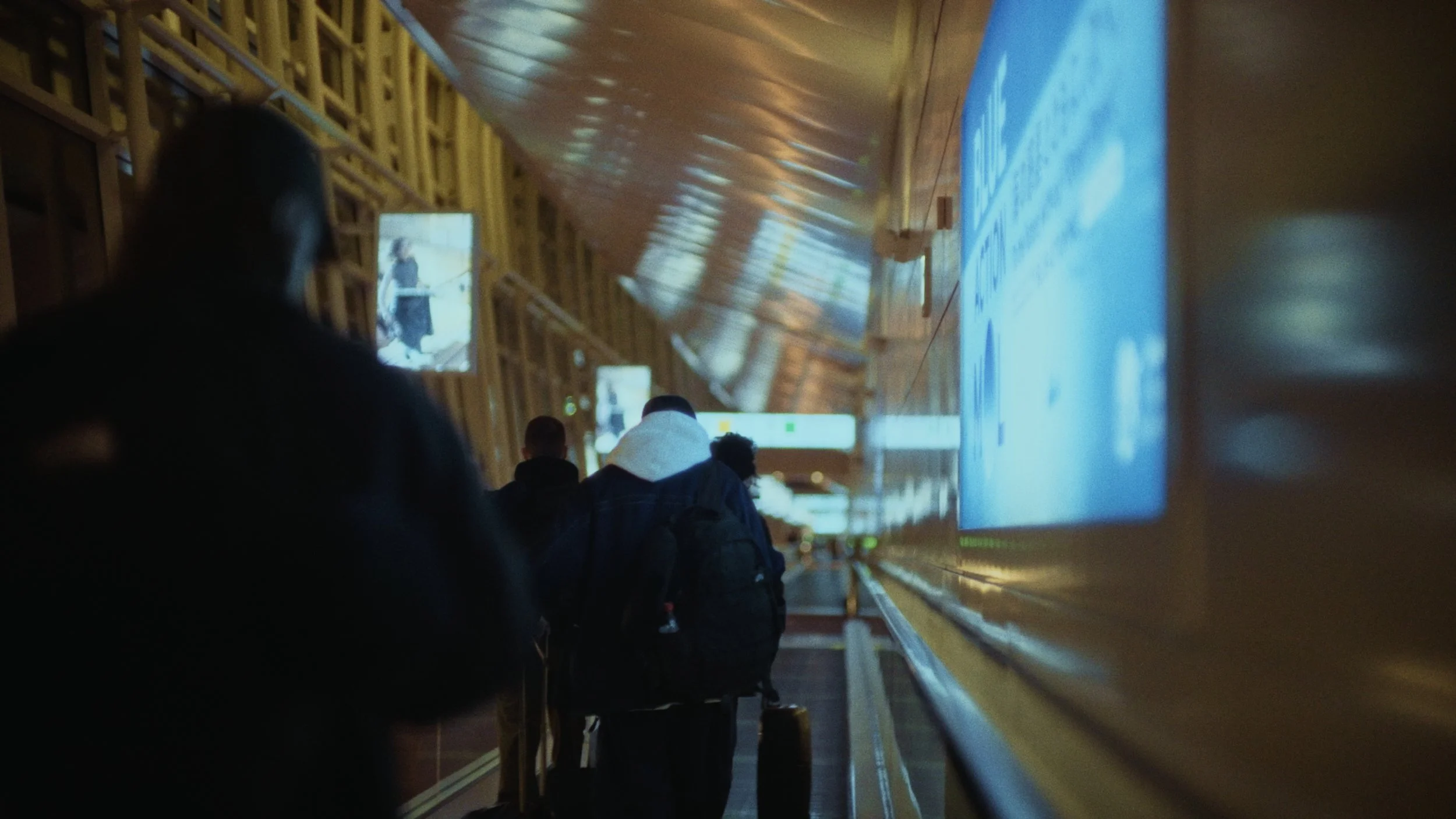 People walking in an airport terminal with wooden architectural features, large digital display screens, and a bright, modern atmosphere.