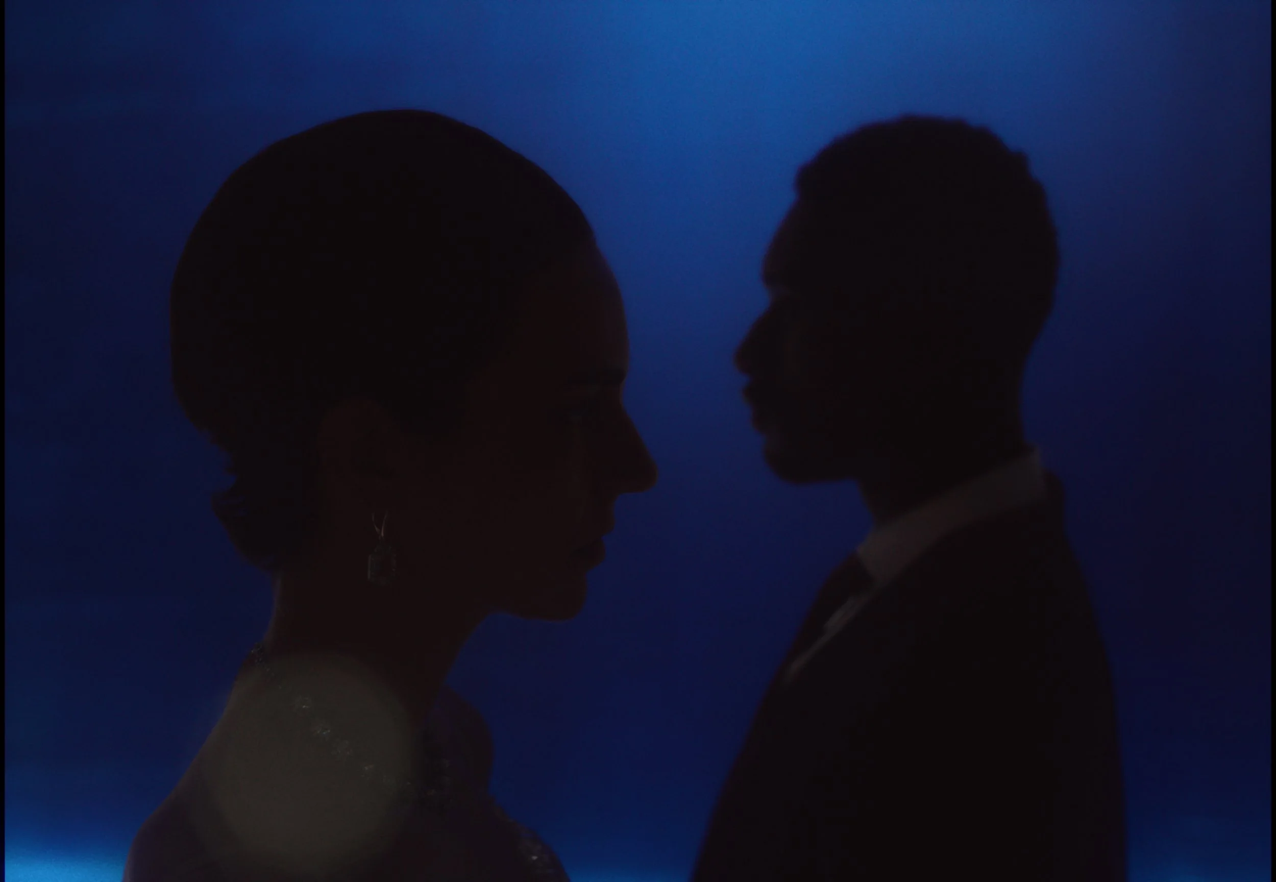 Silhouettes of a man and a woman facing each other against a dark blue background.