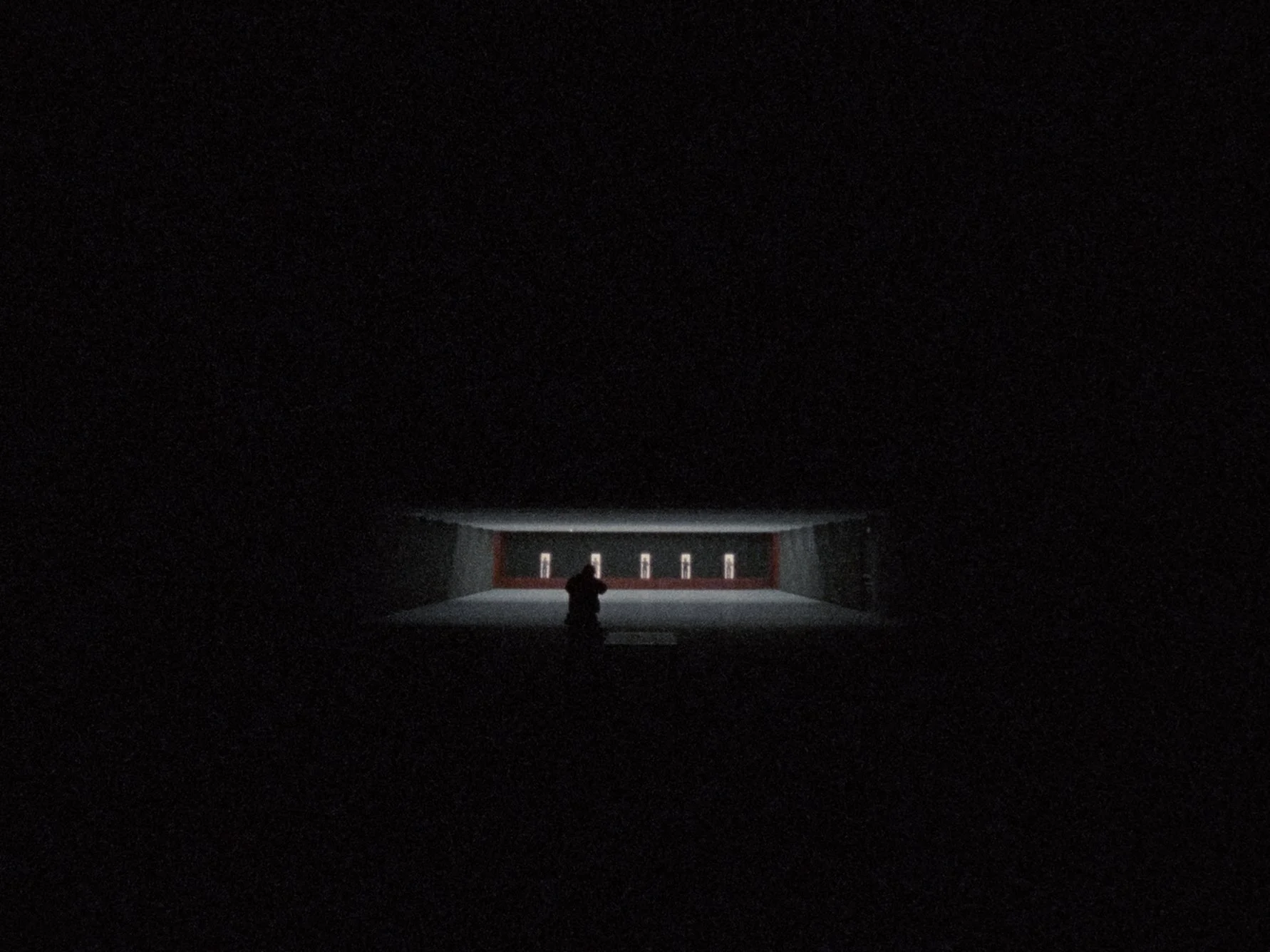 A dark theater with a person sitting alone, facing a blank stage with a row of seats and illuminated screens at the back.