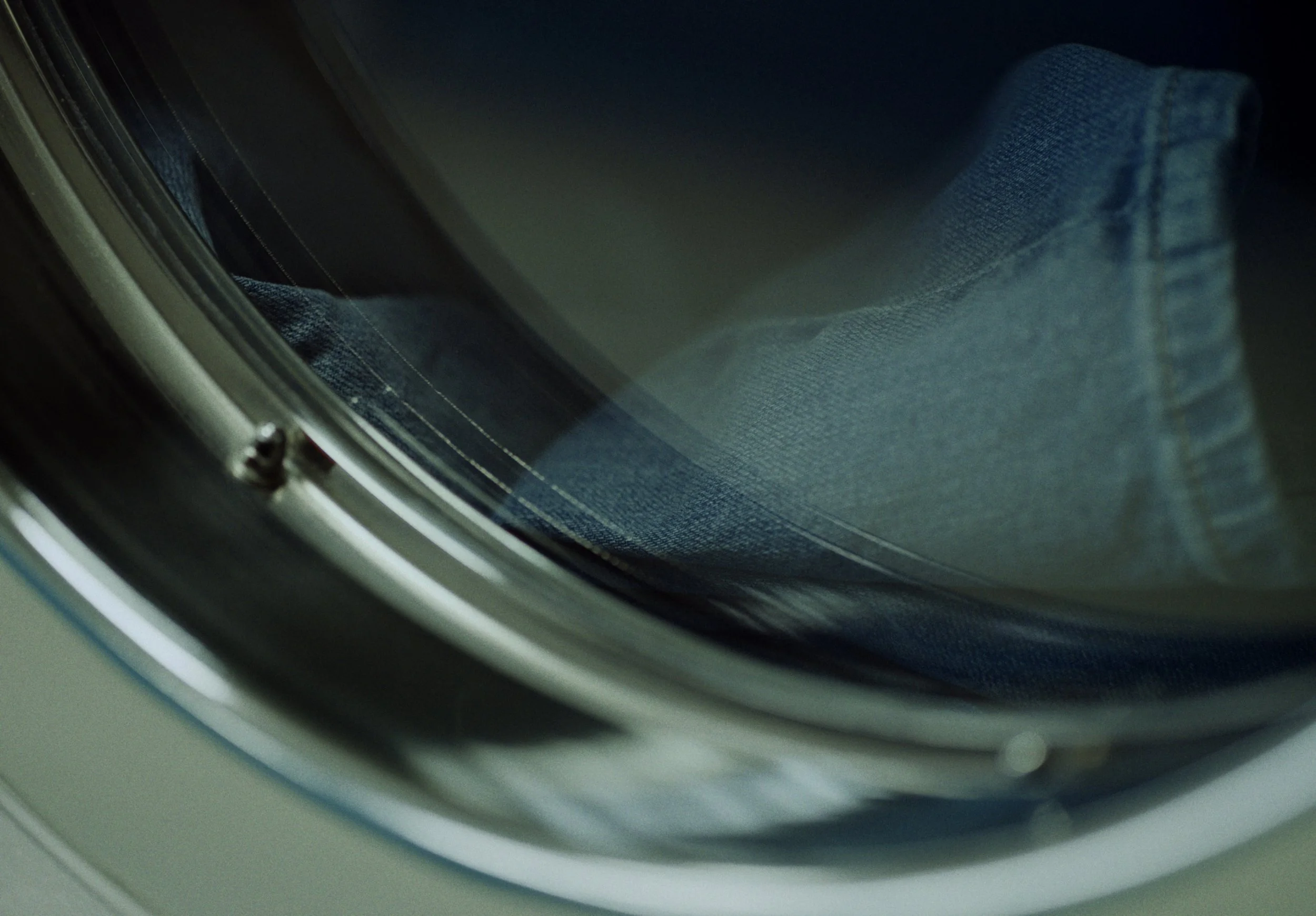 Close-up of the inside of a washing machine door, showing the drum and part of a person’s jeans.