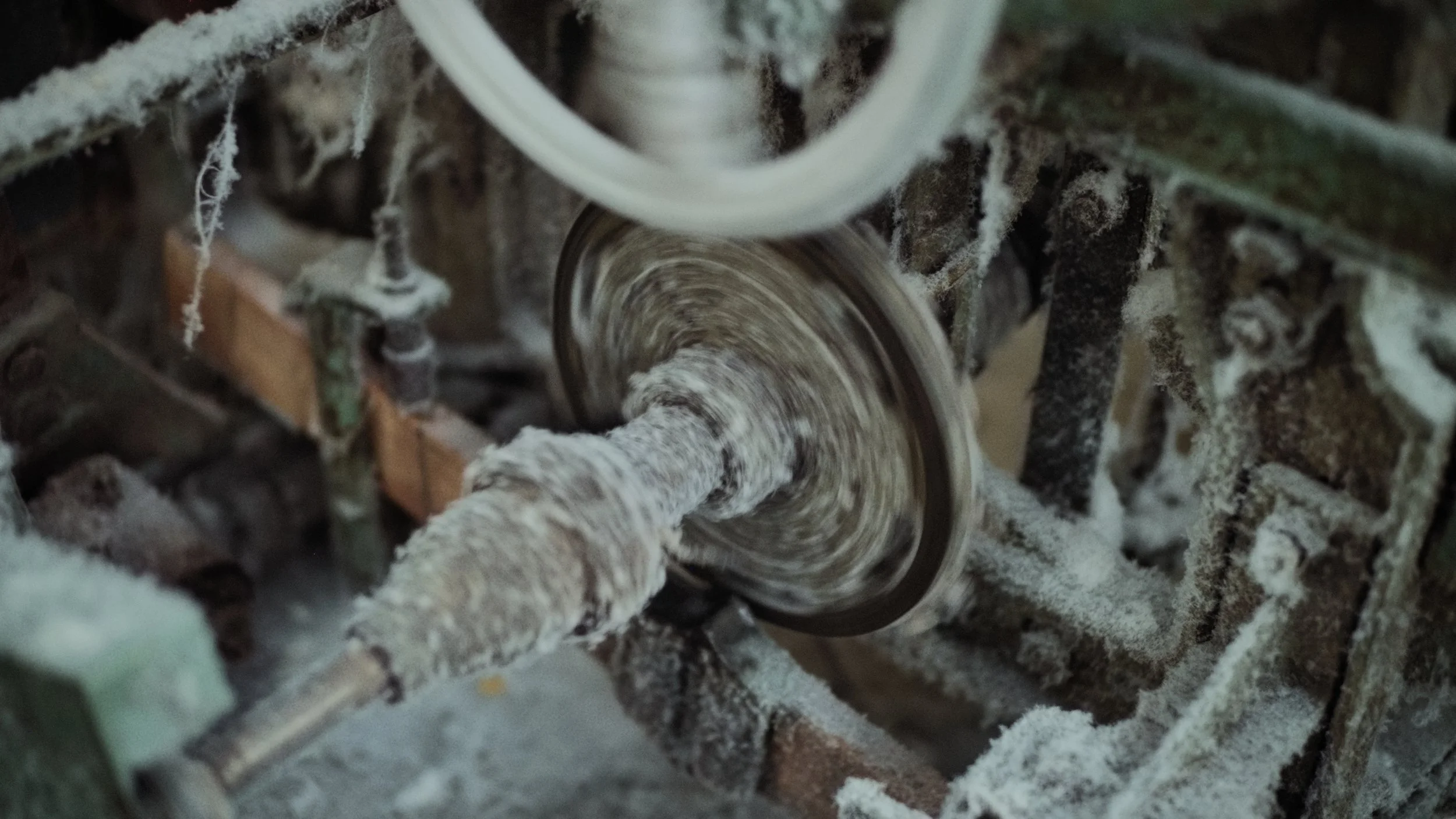 Close-up image of a dusty and corroded metal pipe and machinery, with some cobwebs and dust particles visible on the surface.