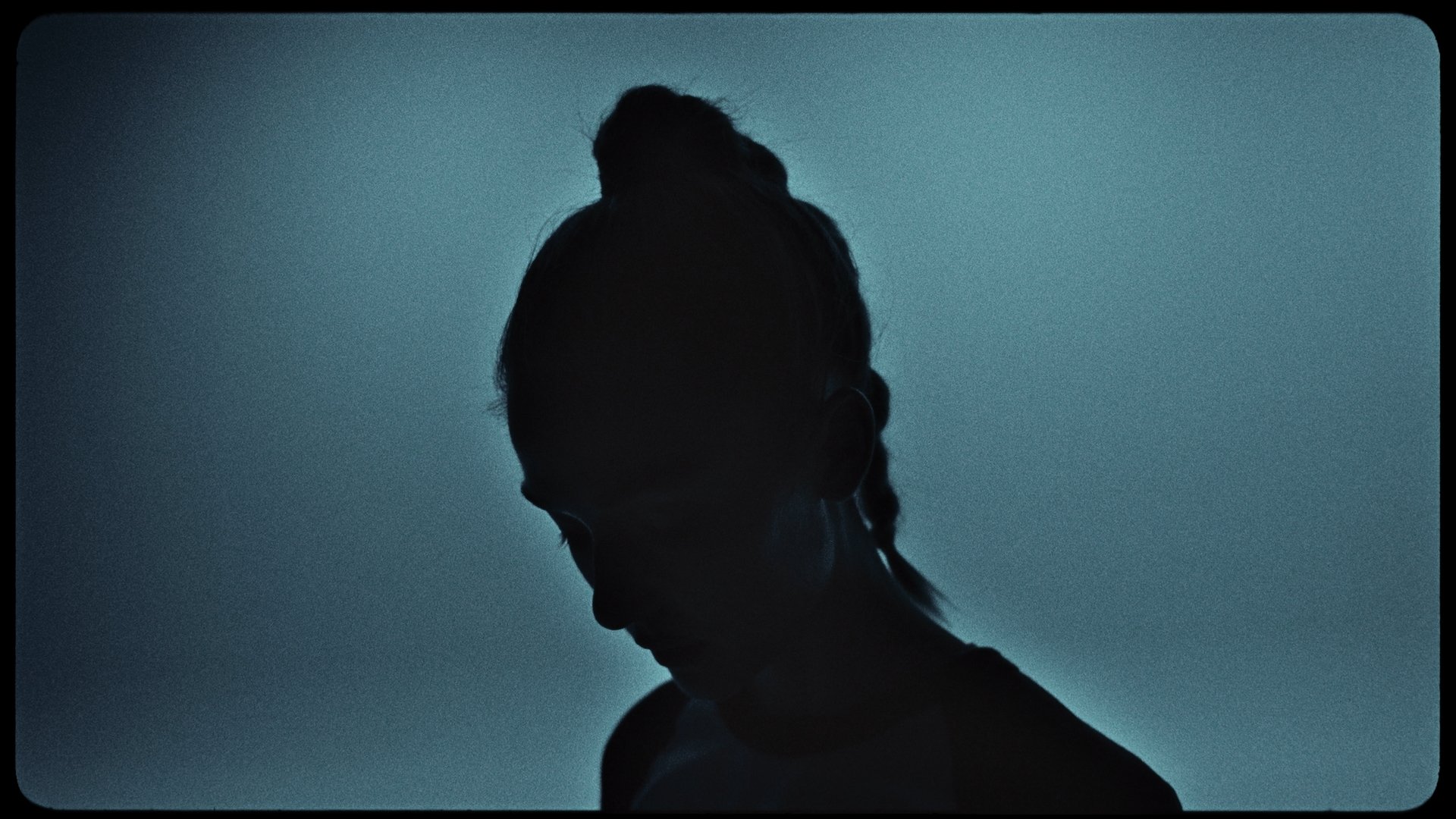 Silhouette of a person with braided hair and glasses, looking downward against a teal background.