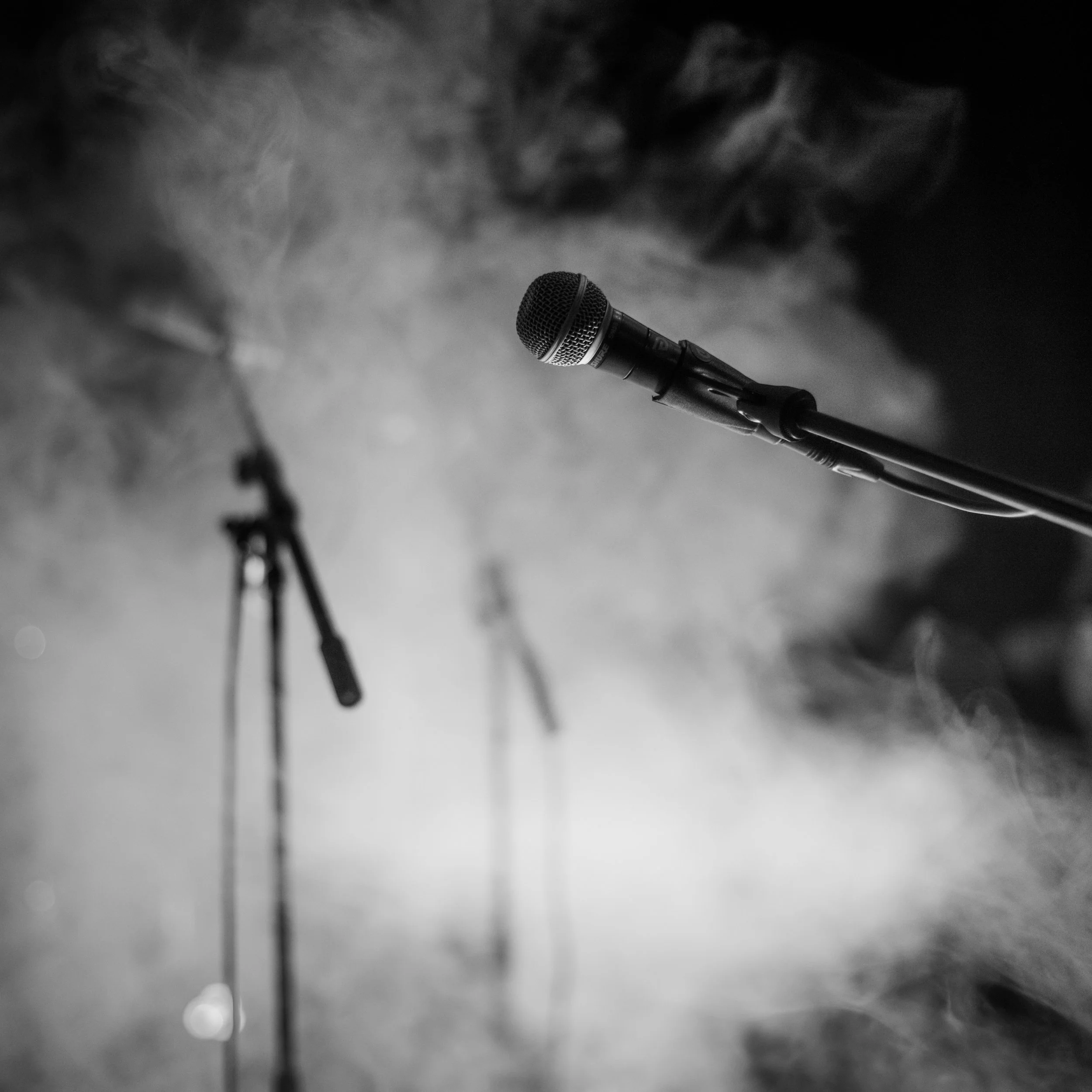 A microphone on a stand in front of a foggy or smoky background, captured in black and white.