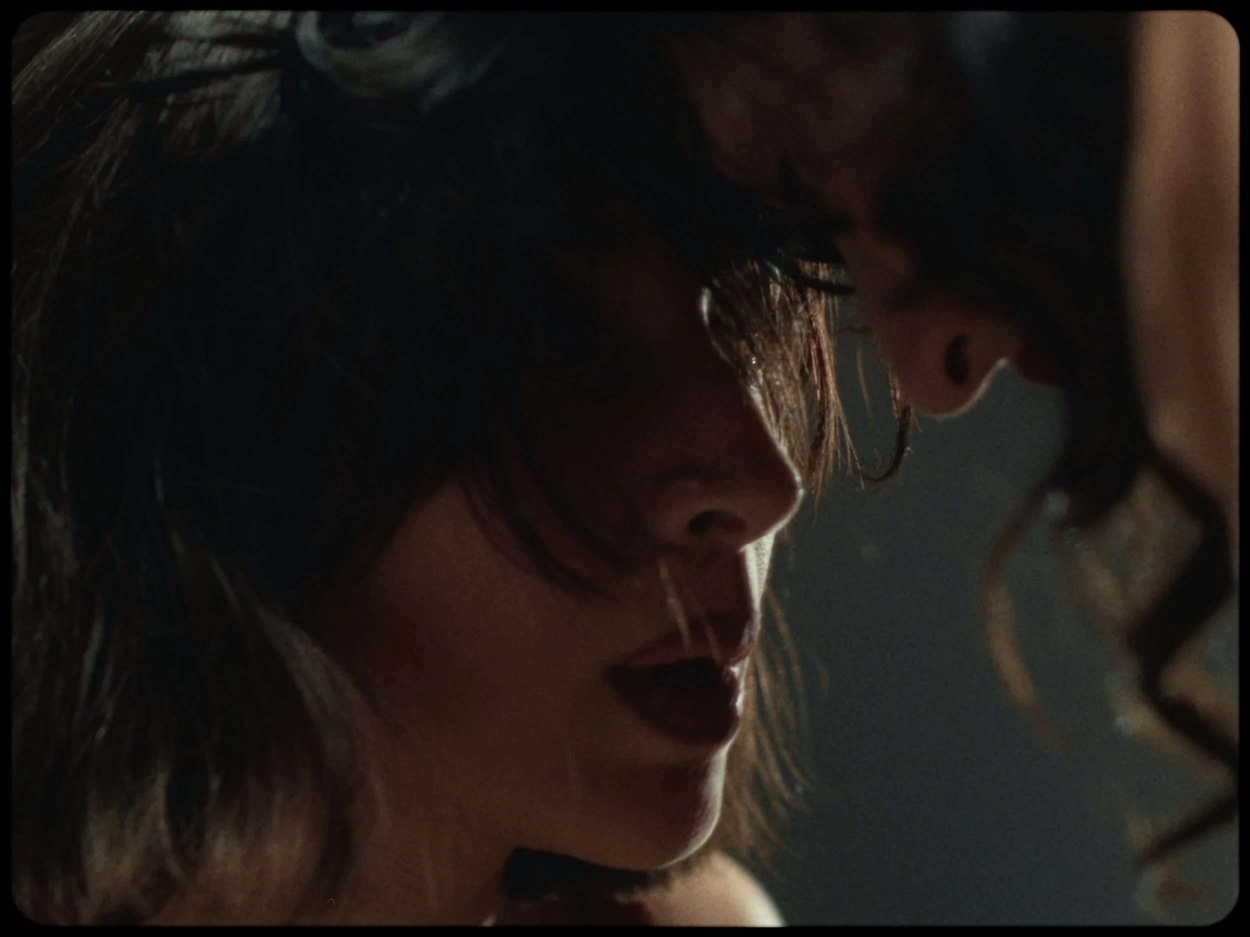 Close-up of a woman's face as she is lying down, with long dark hair and a slightly open mouth, in a dimly lit environment.